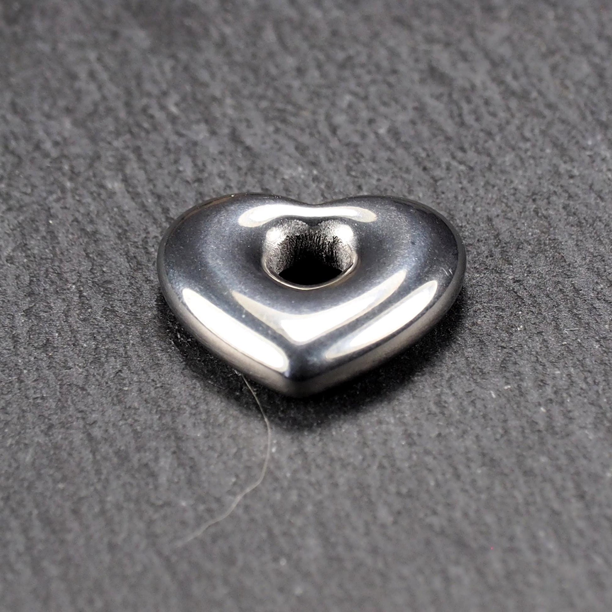 Herzförmiger, silberfarben glänzender Metallanhänger mit glatter Oberfläche und mittigem rundem Fädelloch.