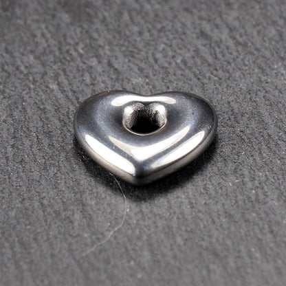 Herzförmiger, silberfarben glänzender Metallanhänger mit glatter Oberfläche und mittigem rundem Fädelloch.