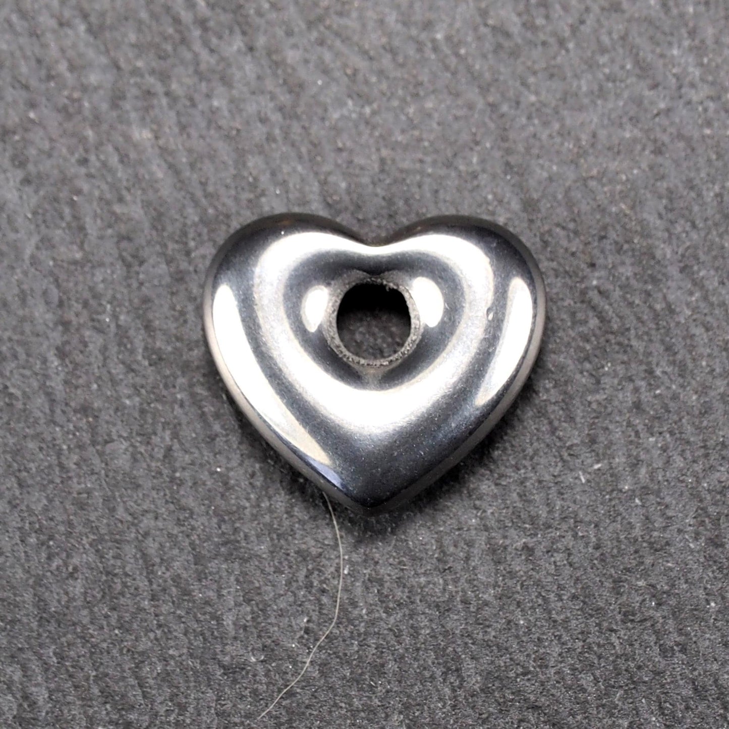 Herzförmiger, silberfarben glänzender Metallanhänger mit glatter Oberfläche und mittigem rundem Fädelloch.