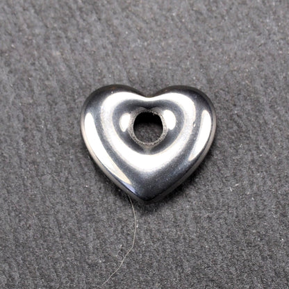 Herzförmiger, silberfarben glänzender Metallanhänger mit glatter Oberfläche und mittigem rundem Fädelloch.