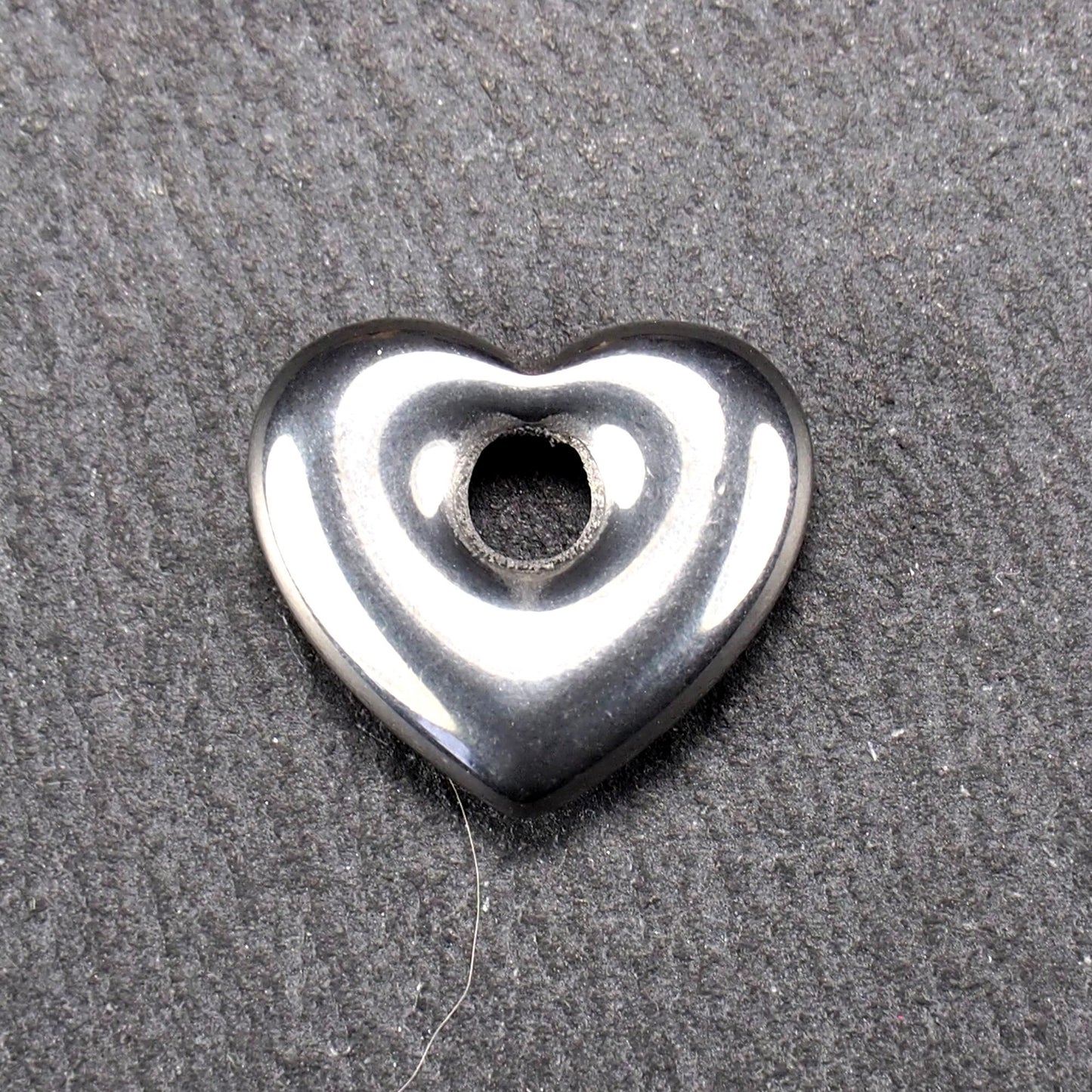 Herzförmiger, silberfarben glänzender Metallanhänger mit glatter Oberfläche und mittigem rundem Fädelloch.