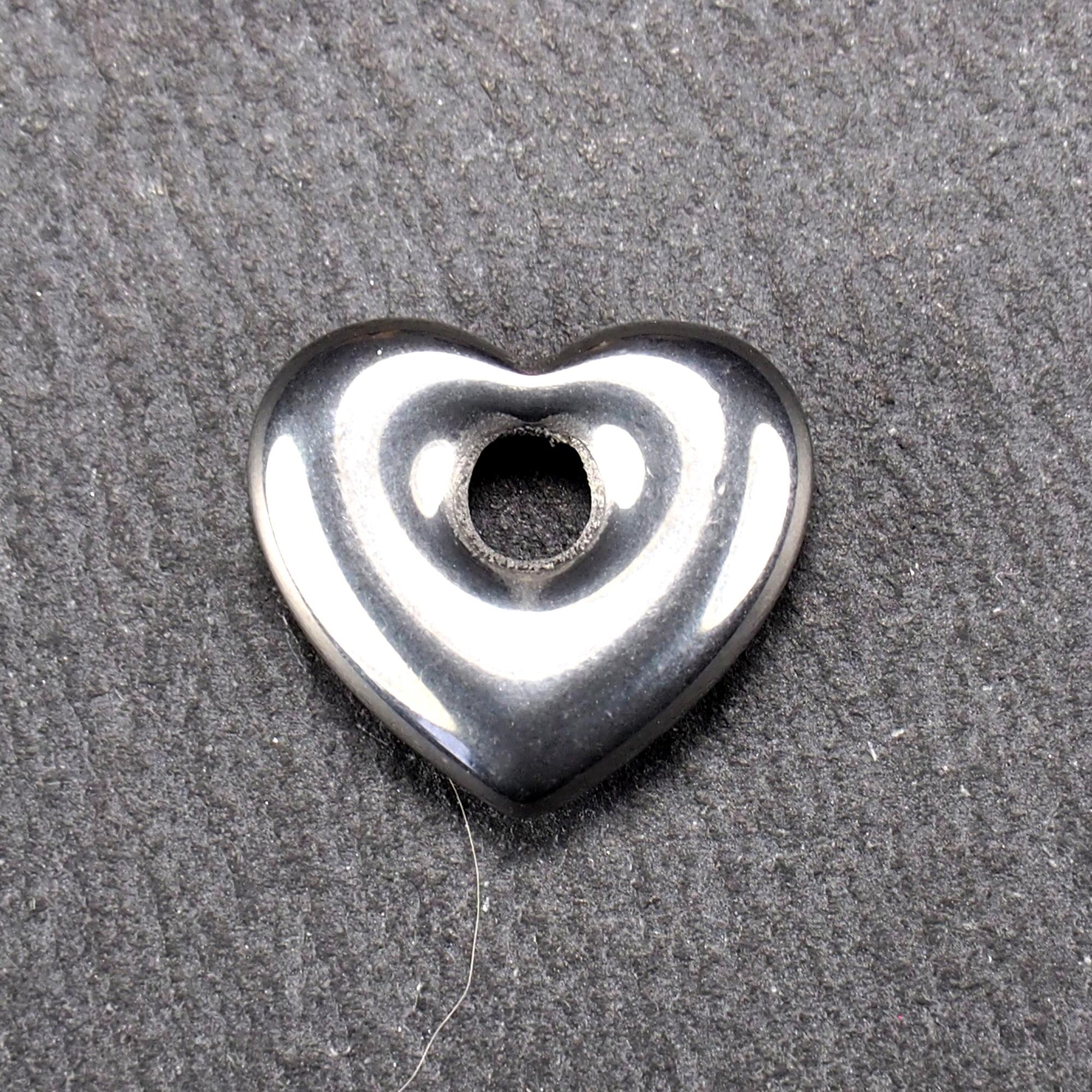Herzförmiger, silberfarben glänzender Metallanhänger mit glatter Oberfläche und mittigem rundem Fädelloch.