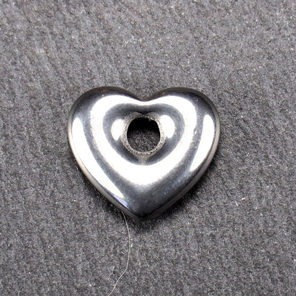 Herzförmiger, silberfarben glänzender Metallanhänger mit glatter Oberfläche und mittigem rundem Fädelloch.