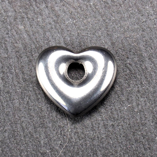 Herzförmiger, silberfarben glänzender Metallanhänger mit glatter Oberfläche und mittigem rundem Fädelloch.