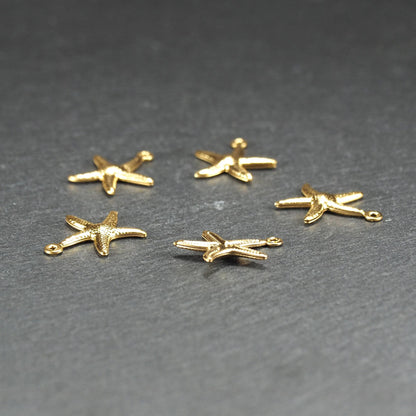 Fünf goldfarbene, flache Seestern-Anhänger mit reliefartiger, strukturierter und glänzender Oberfläche, jeweils mit kleiner runder Öse zum Aufhängen.