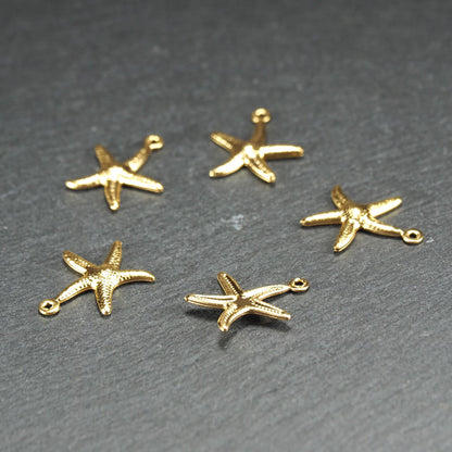 Fünf goldfarbene, flache Seestern-Anhänger mit reliefartiger, strukturierter und glänzender Oberfläche, jeweils mit kleiner runder Öse zum Aufhängen.
