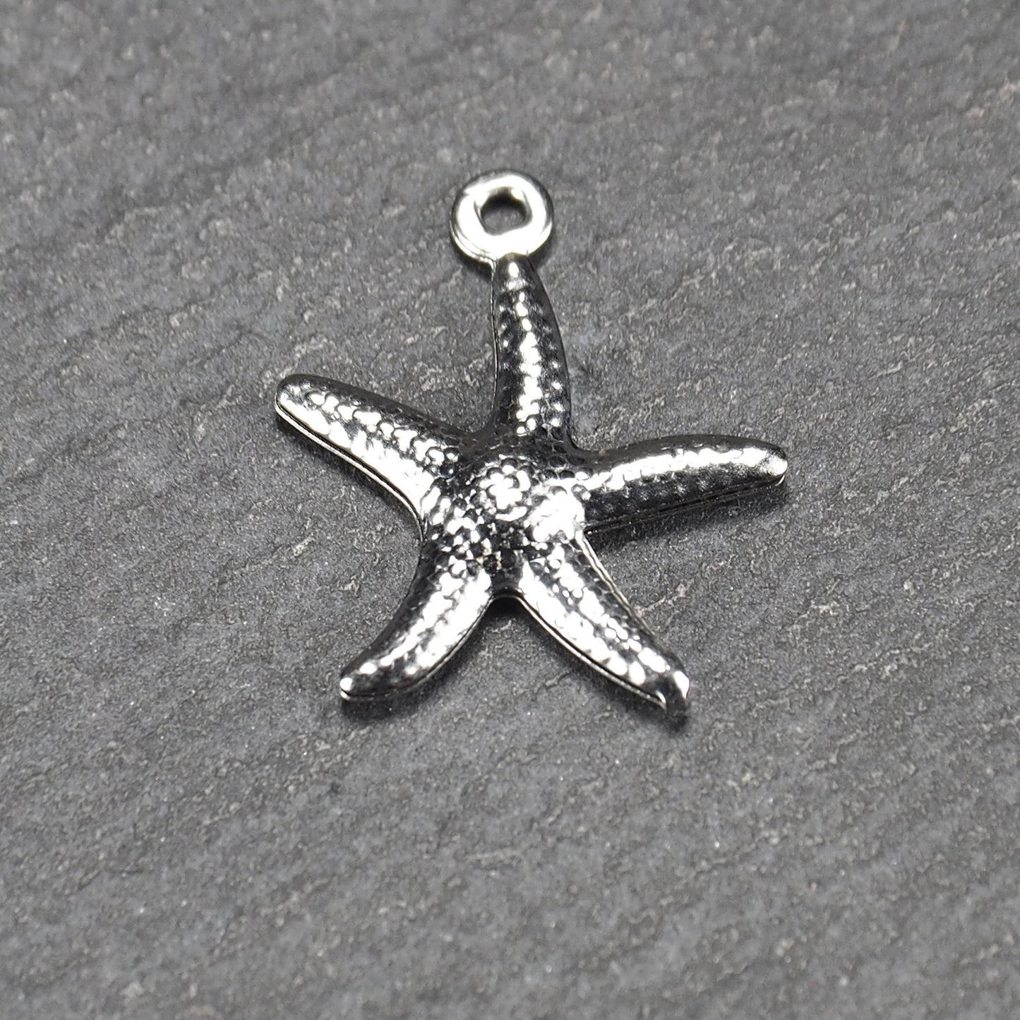 Seestern-Anhänger aus silberfarbenem Metall mit reliefartiger, strukturierter glänzender Oberfläche, fünf Armen und kleiner runder Öse oben.