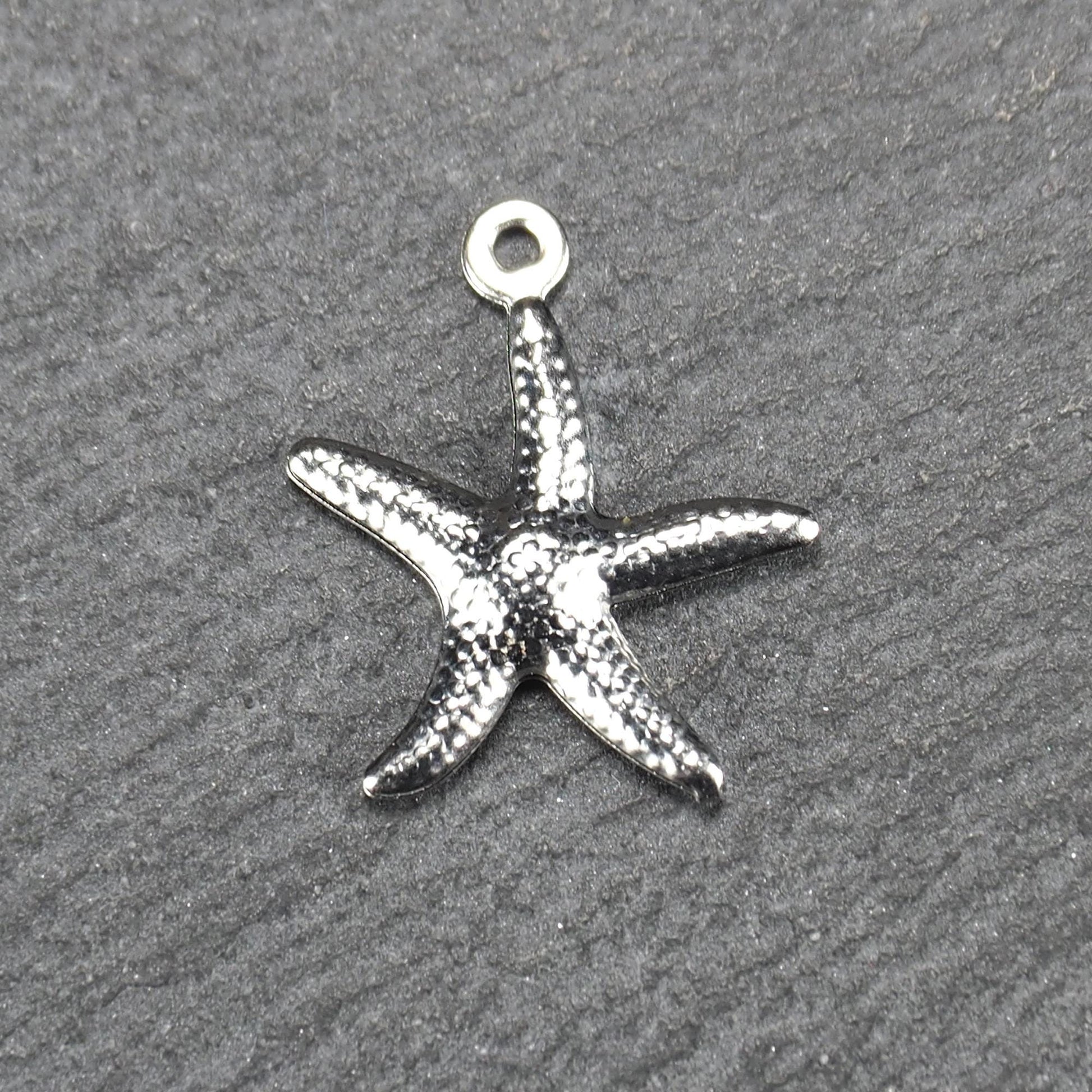 Seestern-Anhänger aus silberfarbenem Metall mit reliefartiger, strukturierter glänzender Oberfläche, fünf Armen und kleiner runder Öse oben.