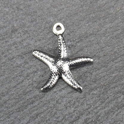 Seestern-Anhänger aus silberfarbenem Metall mit reliefartiger, strukturierter glänzender Oberfläche, fünf Armen und kleiner runder Öse oben.