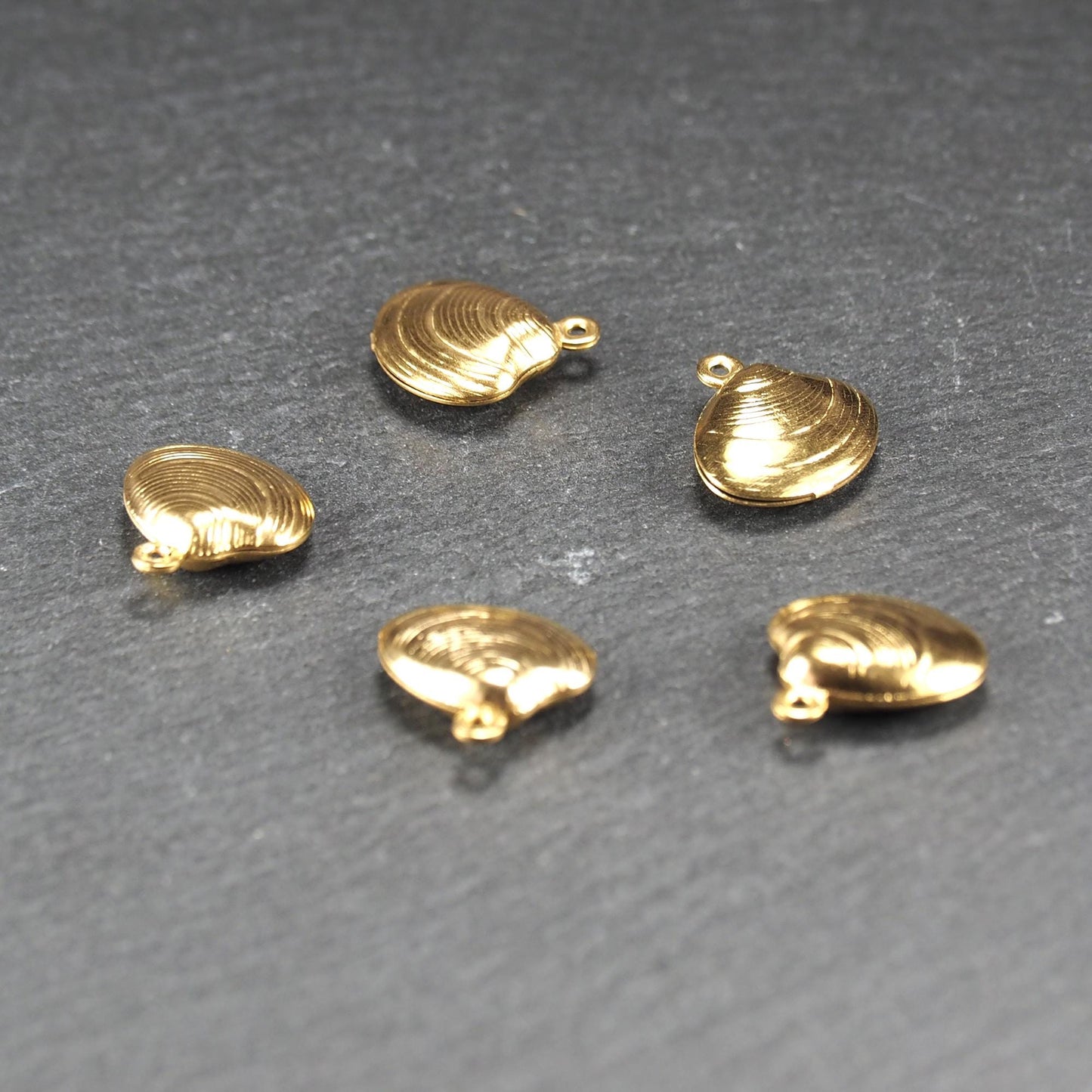 Kleiner muschelförmiger Anhänger, goldfarbene glänzende Oberfläche mit konzentrischen Rillen und integrierter Öse oben.