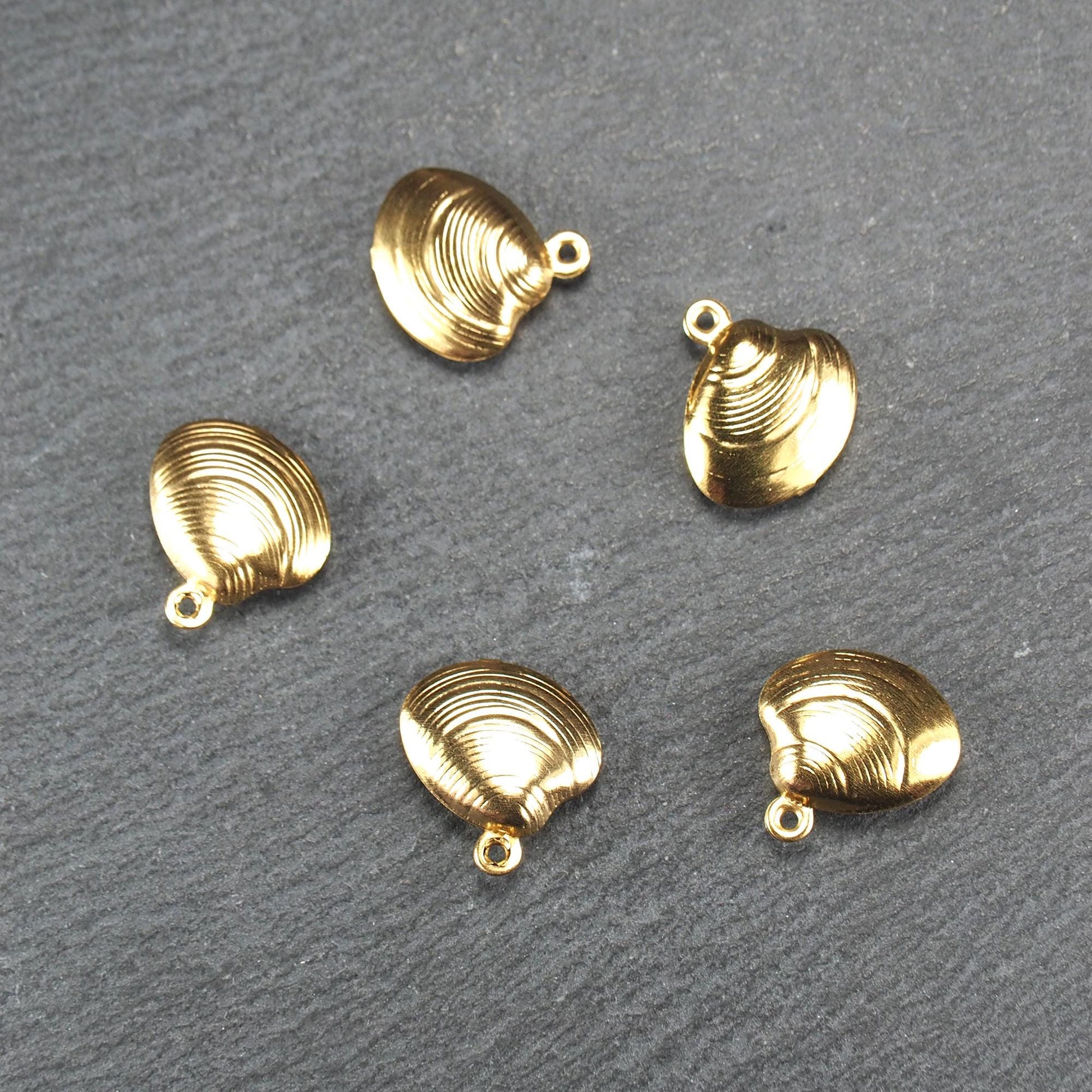Kleiner muschelförmiger Anhänger, goldfarbene glänzende Oberfläche mit konzentrischen Rillen und integrierter Öse oben.