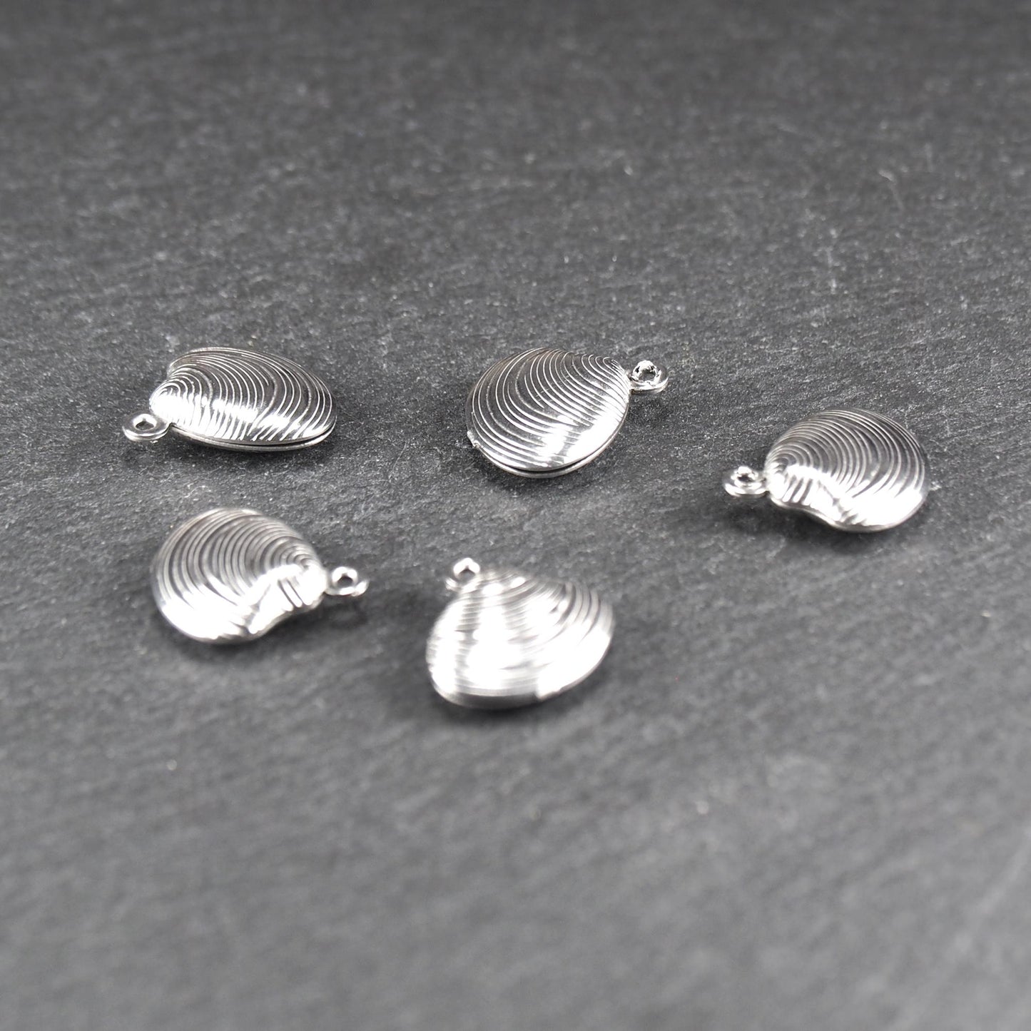 Muschelförmiger silberfarbener Anhänger mit polierter, glänzender Oberfläche, konzentrisch geriffelten Rillen und integrierter runder Öse oben.