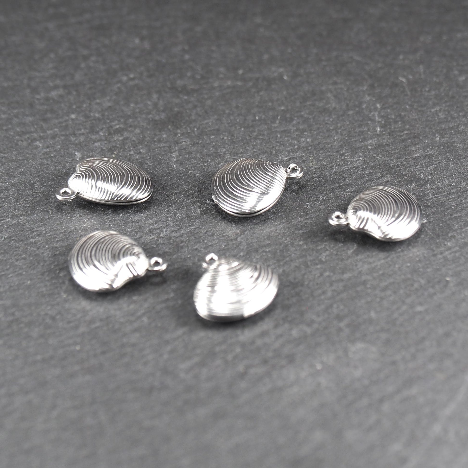 Muschelförmiger silberfarbener Anhänger mit polierter, glänzender Oberfläche, konzentrisch geriffelten Rillen und integrierter runder Öse oben.