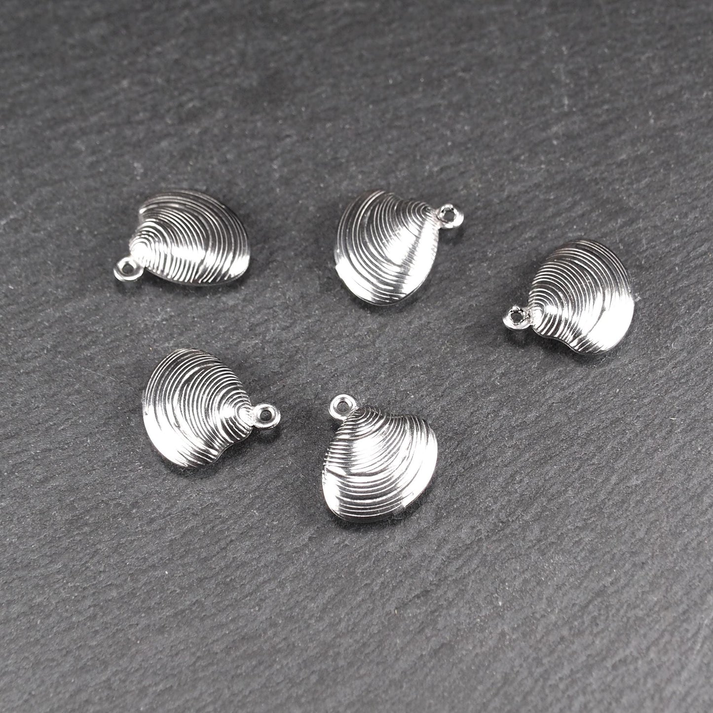 Muschelförmiger silberfarbener Anhänger mit polierter, glänzender Oberfläche, konzentrisch geriffelten Rillen und integrierter runder Öse oben.