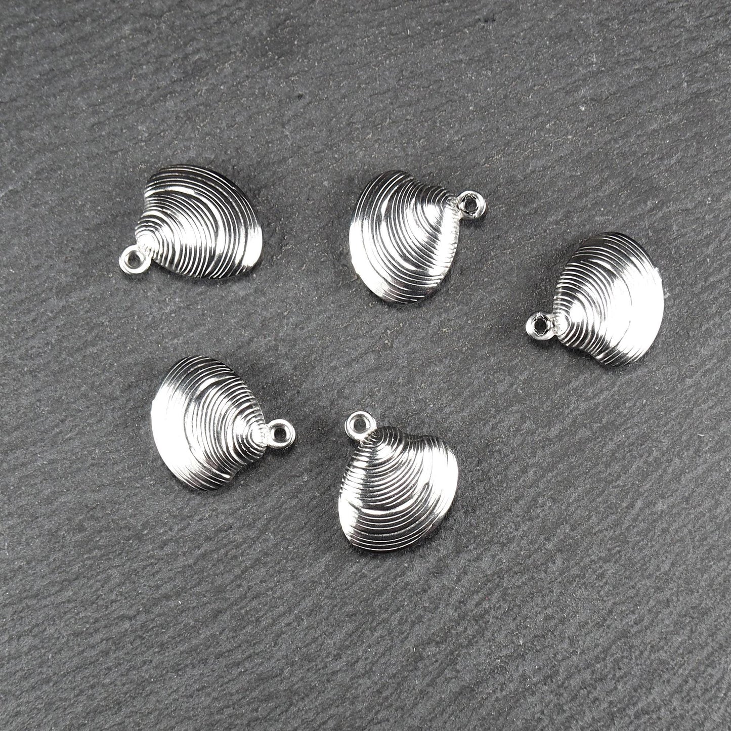 Muschelförmiger silberfarbener Anhänger mit polierter, glänzender Oberfläche, konzentrisch geriffelten Rillen und integrierter runder Öse oben.