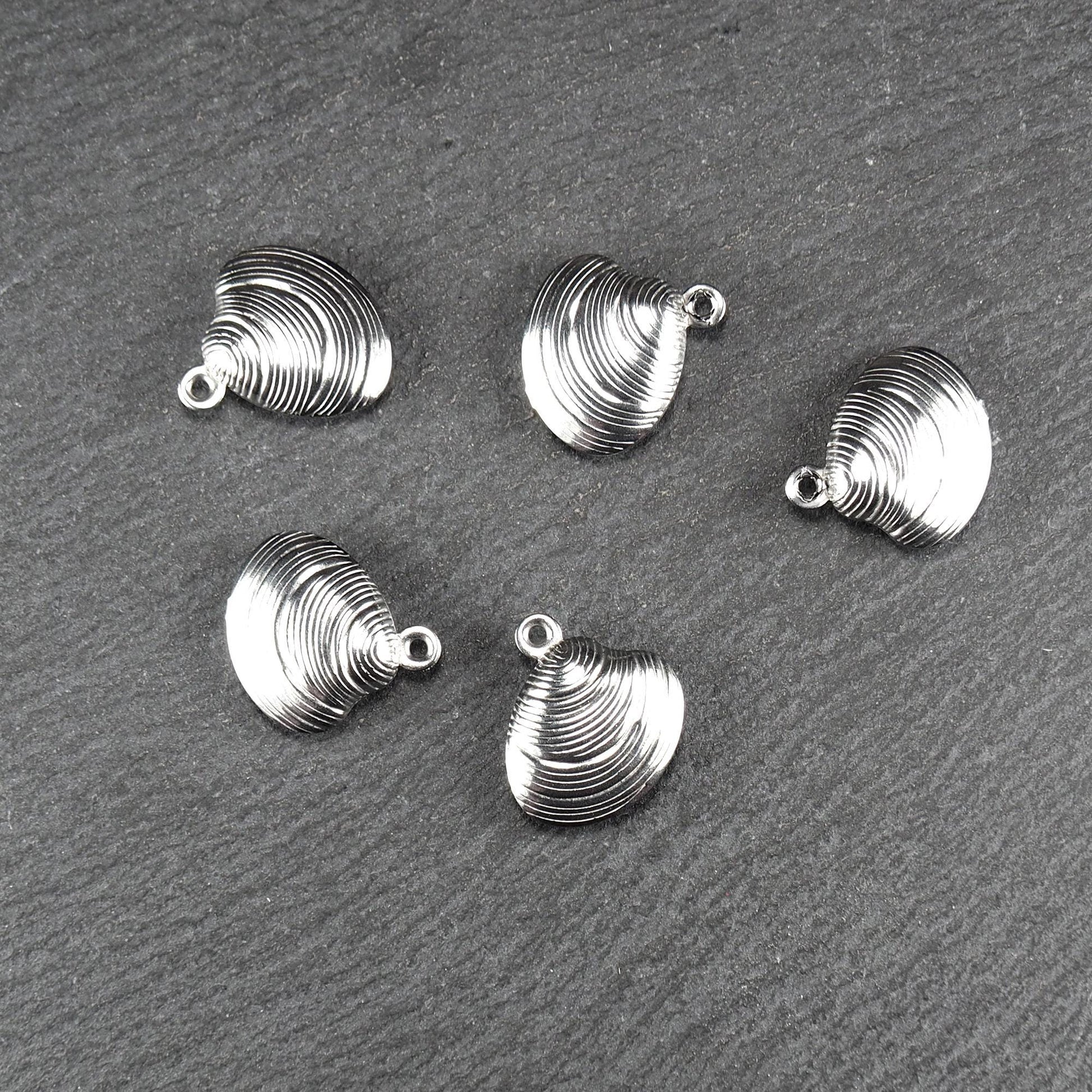 Muschelförmiger silberfarbener Anhänger mit polierter, glänzender Oberfläche, konzentrisch geriffelten Rillen und integrierter runder Öse oben.