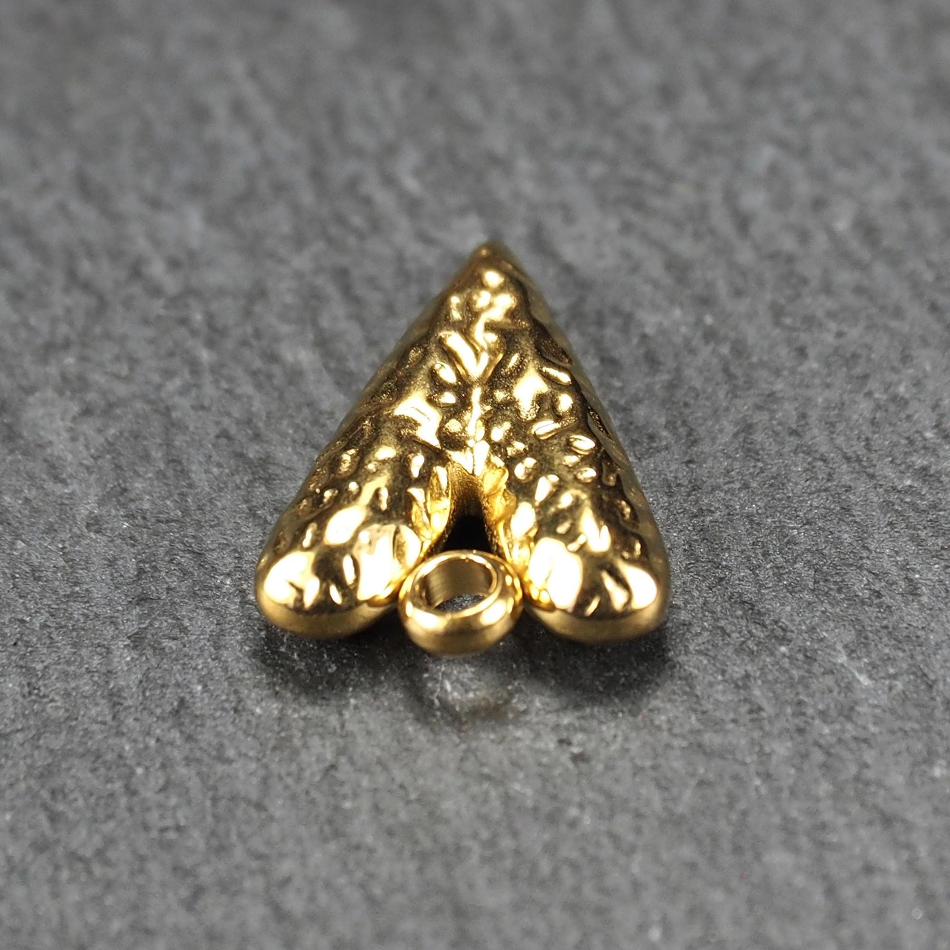 Herzförmiger, vergoldeter Anhänger mit strukturierter Reliefoberfläche, spitz zulaufender Form und integrierter Öse oben.