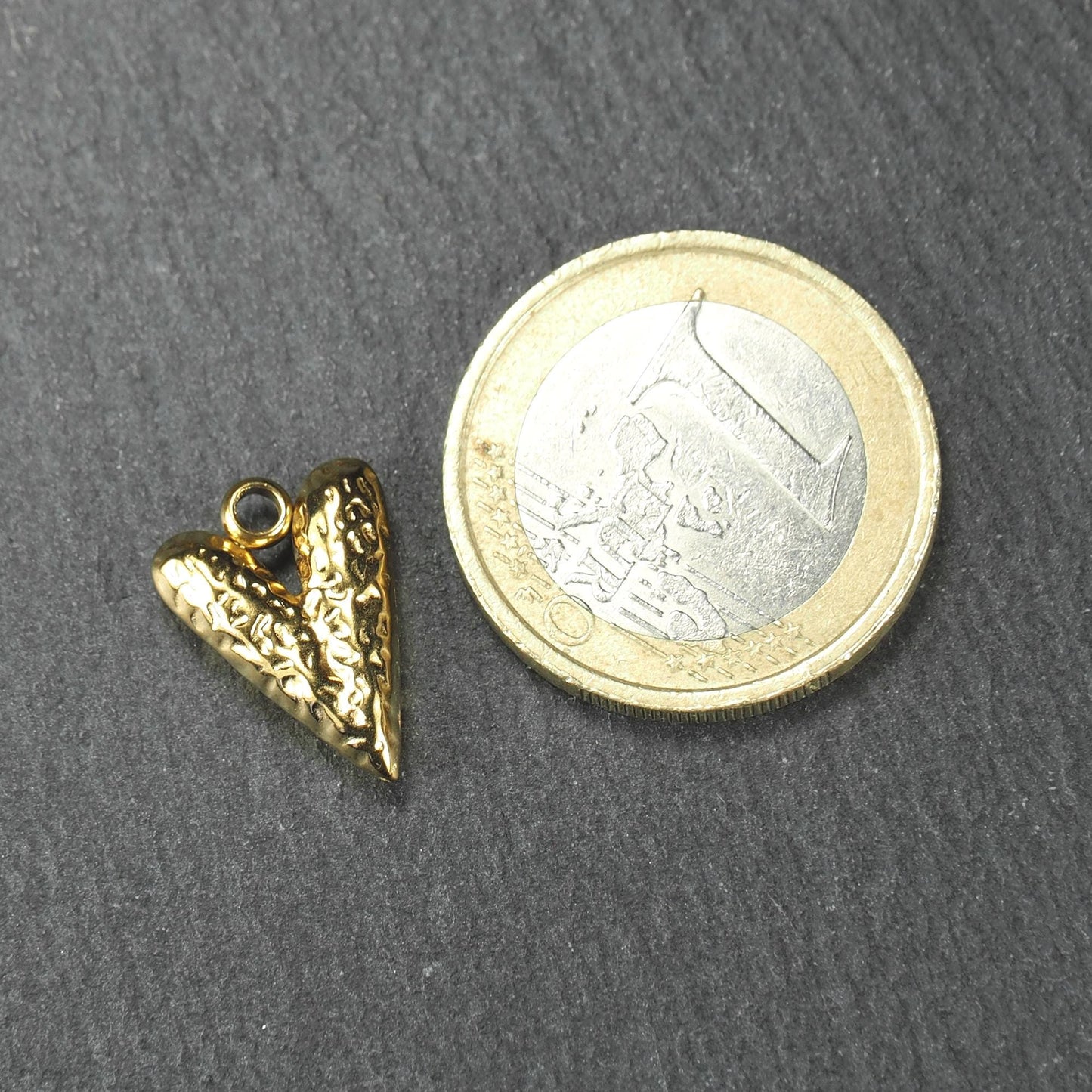 Herzförmiger goldfarbener Anhänger mit reliefierter, glänzender Oberfläche, integrierter Öse oben, neben einer 1‑Euro‑Münze.