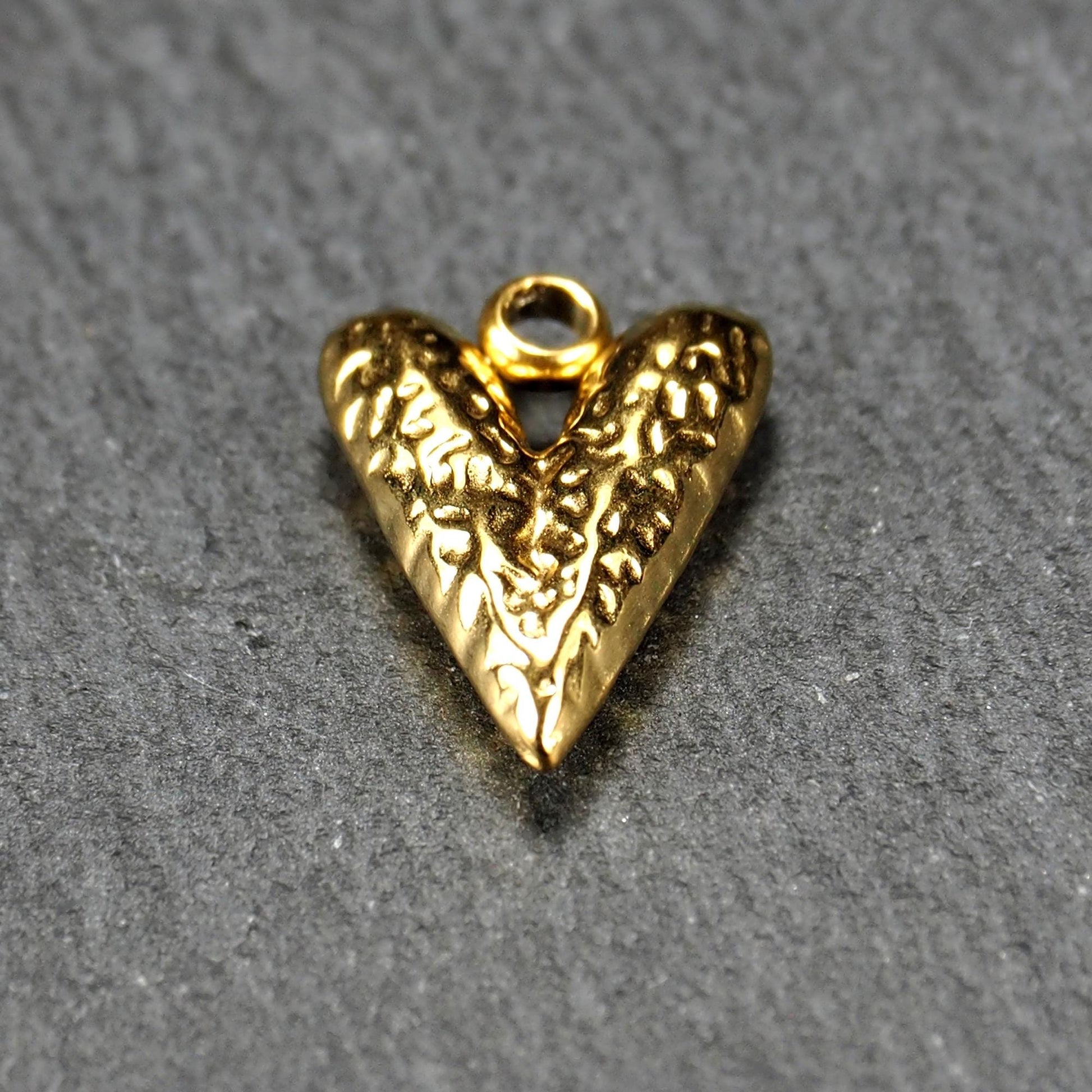 Herzförmiger, vergoldeter Anhänger mit strukturierter Reliefoberfläche, spitz zulaufender Form und integrierter Öse oben.