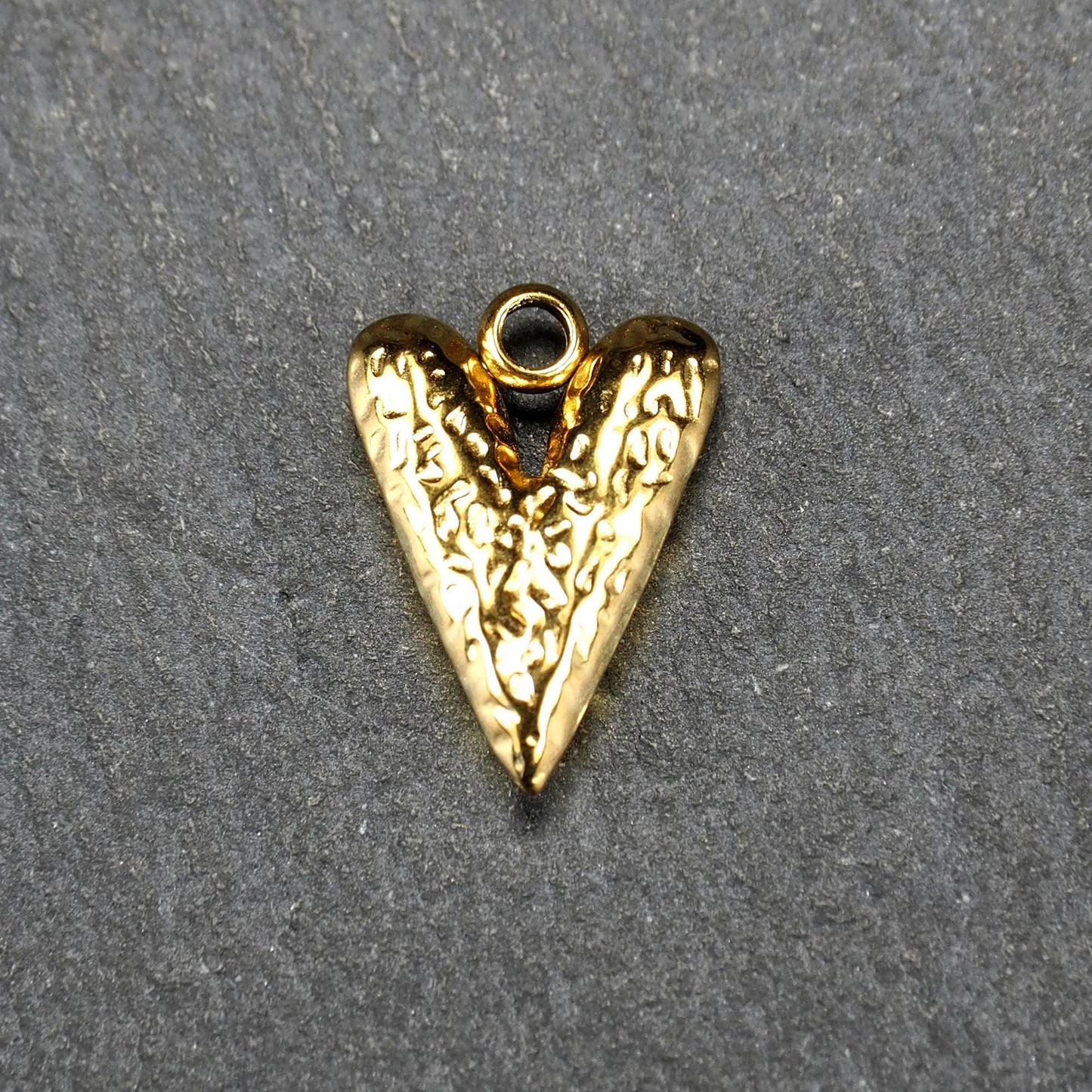 Herzförmiger, vergoldeter Anhänger mit strukturierter Reliefoberfläche, spitz zulaufender Form und integrierter Öse oben.