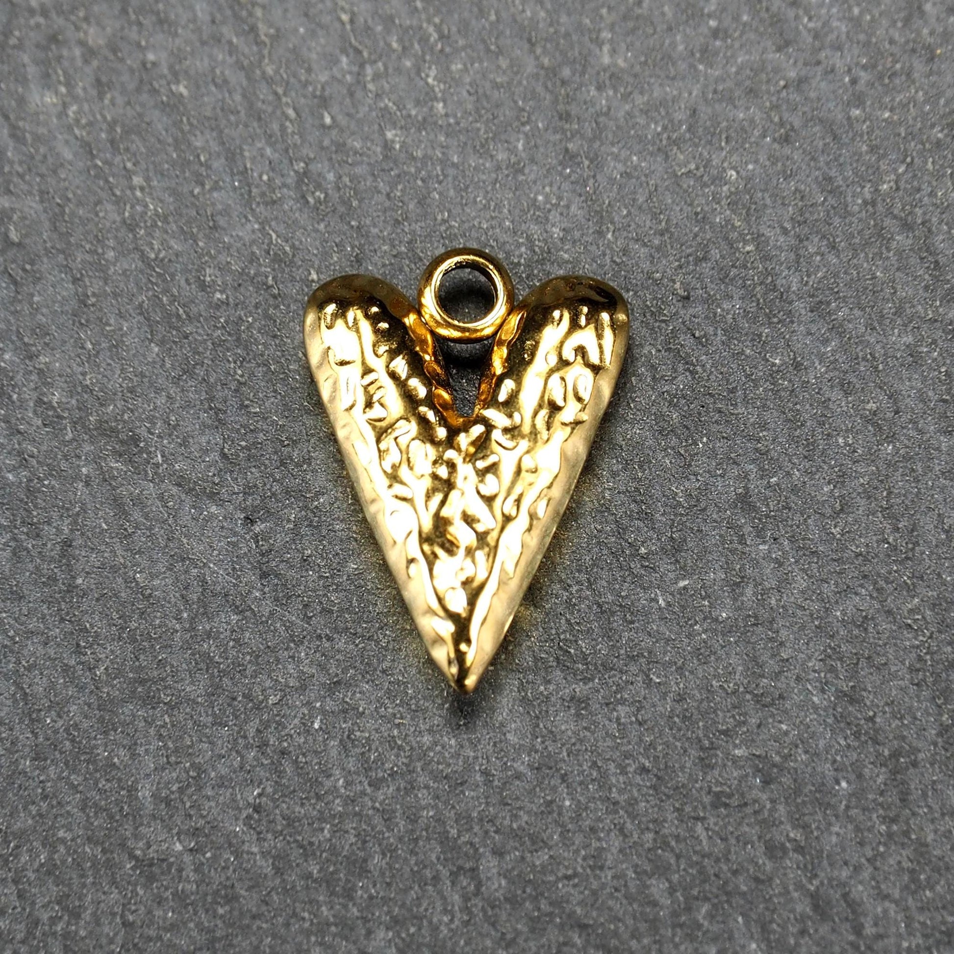 Herzförmiger, vergoldeter Anhänger mit strukturierter Reliefoberfläche, spitz zulaufender Form und integrierter Öse oben.
