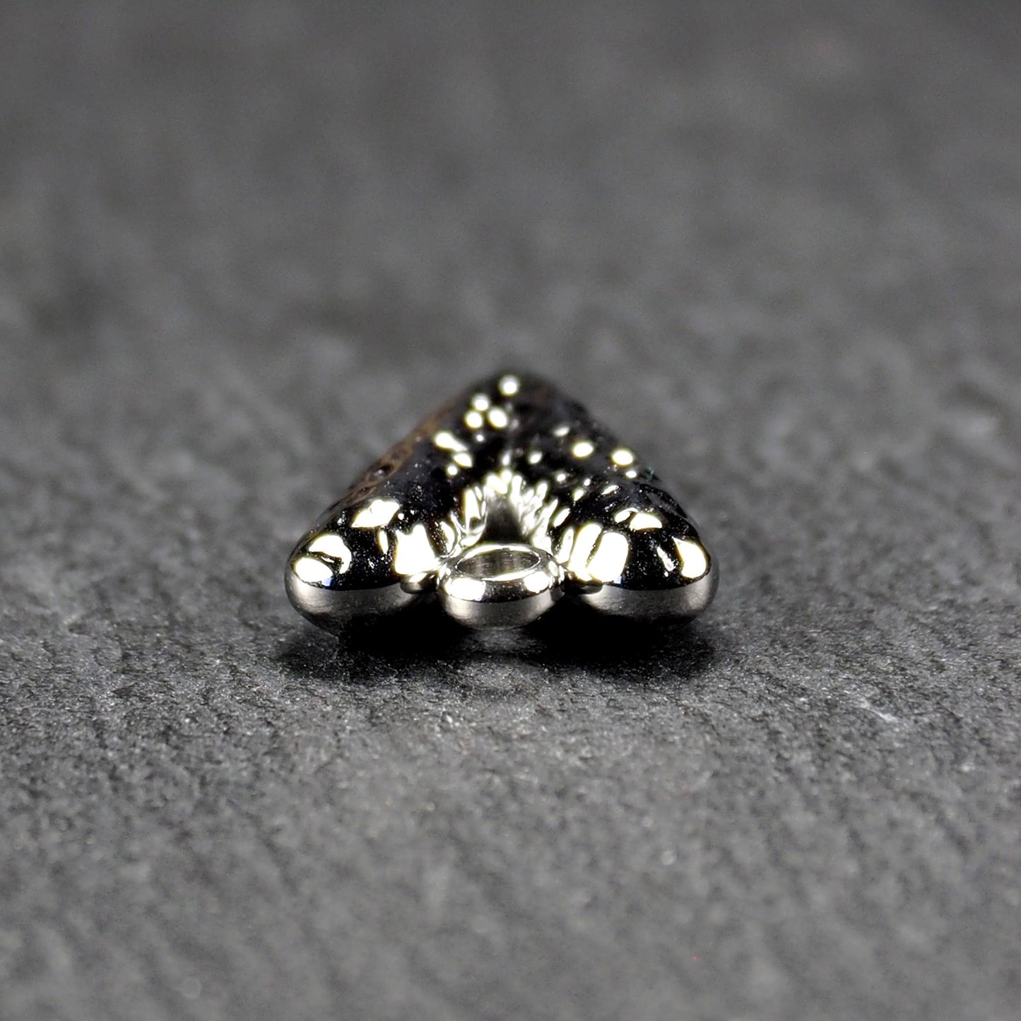 Herzanhänger, silberfarbig hochglänzend mit reliefartiger Oberfläche, spitz zulaufender Unterseite und integrierter runder Öse.