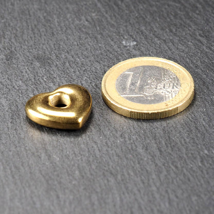 Goldfarbener, polierter Herzanhänger mit runder offener Mittelöffnung und abgerundeten Konturen, neben einer Ein-Euro-Münze als Maßstab.