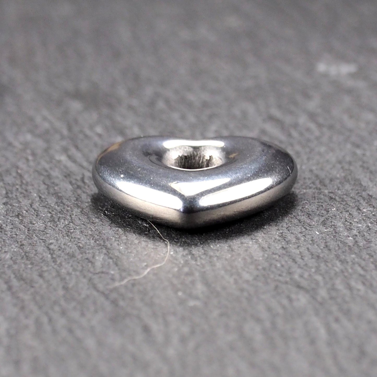 Herzförmiger, silberfarben glänzender Metallanhänger mit glatter Oberfläche und mittigem rundem Fädelloch.