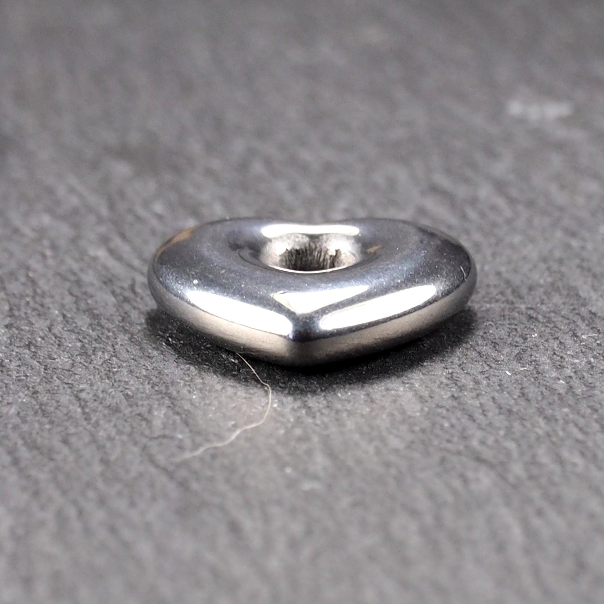 Herzförmiger, silberfarben glänzender Metallanhänger mit glatter Oberfläche und mittigem rundem Fädelloch.