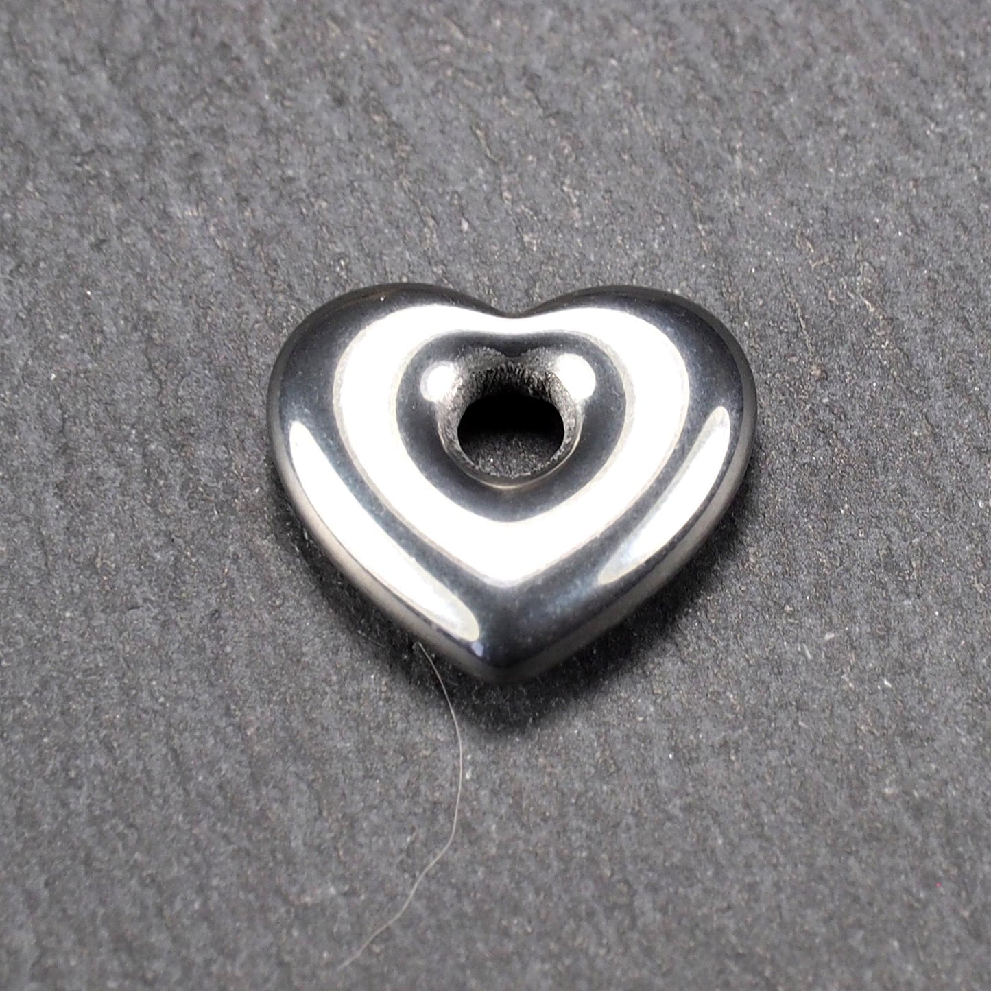 Herzförmiger, silberfarben glänzender Metallanhänger mit glatter Oberfläche und mittigem rundem Fädelloch.