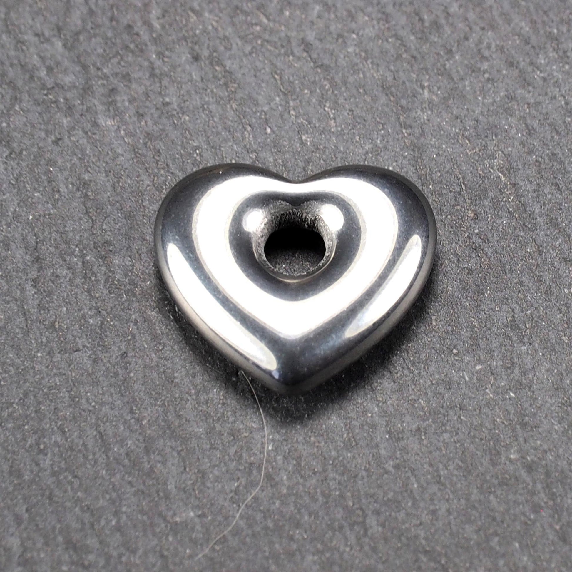 Herzförmiger, silberfarben glänzender Metallanhänger mit glatter Oberfläche und mittigem rundem Fädelloch.