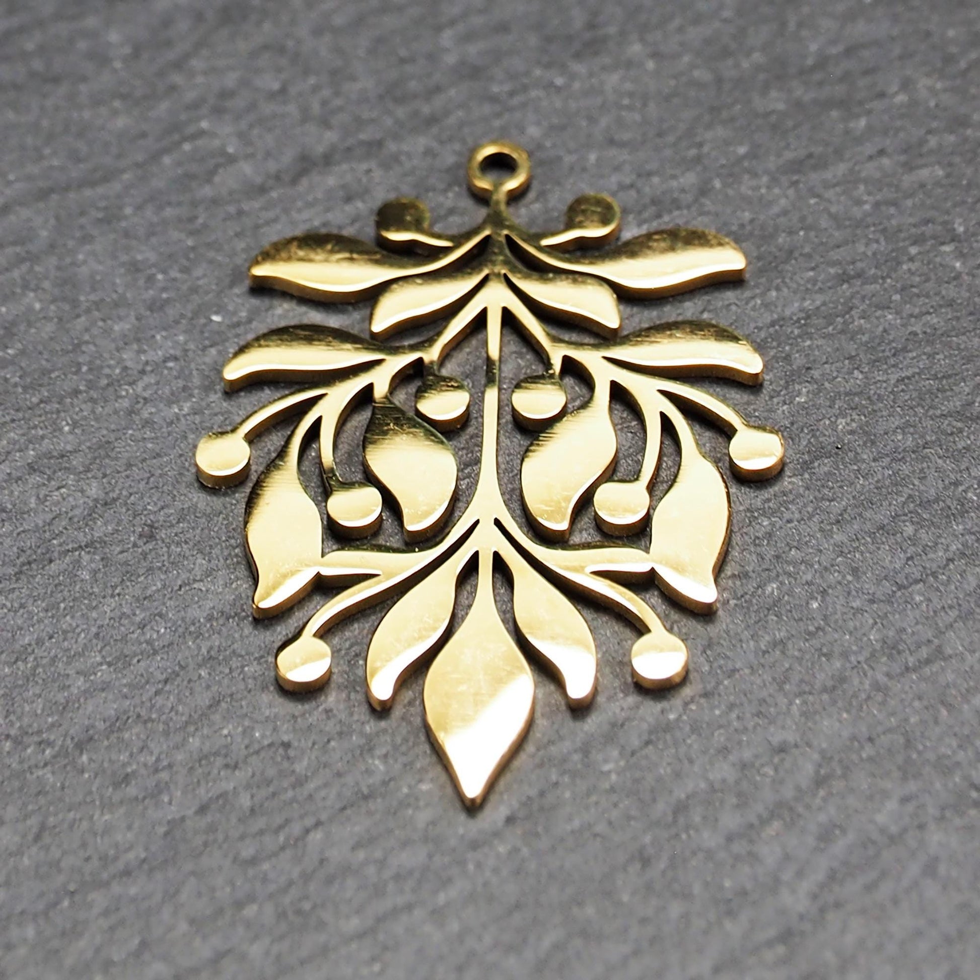 Goldfarbener Metallanhänger mit glänzender Oberfläche, durchbrochenes Zweig- und Beerenmotiv mit stilisierten Blättern und runder Öse oben.