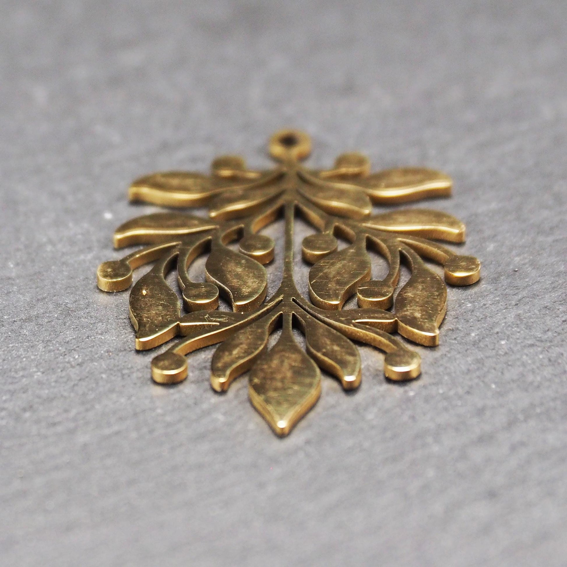 Goldfarbener Metallanhänger mit glänzender Oberfläche, durchbrochenes Zweig- und Beerenmotiv mit stilisierten Blättern und runder Öse oben.