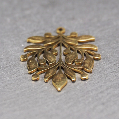 Goldfarbener Metallanhänger mit glänzender Oberfläche, durchbrochenes Zweig- und Beerenmotiv mit stilisierten Blättern und runder Öse oben.