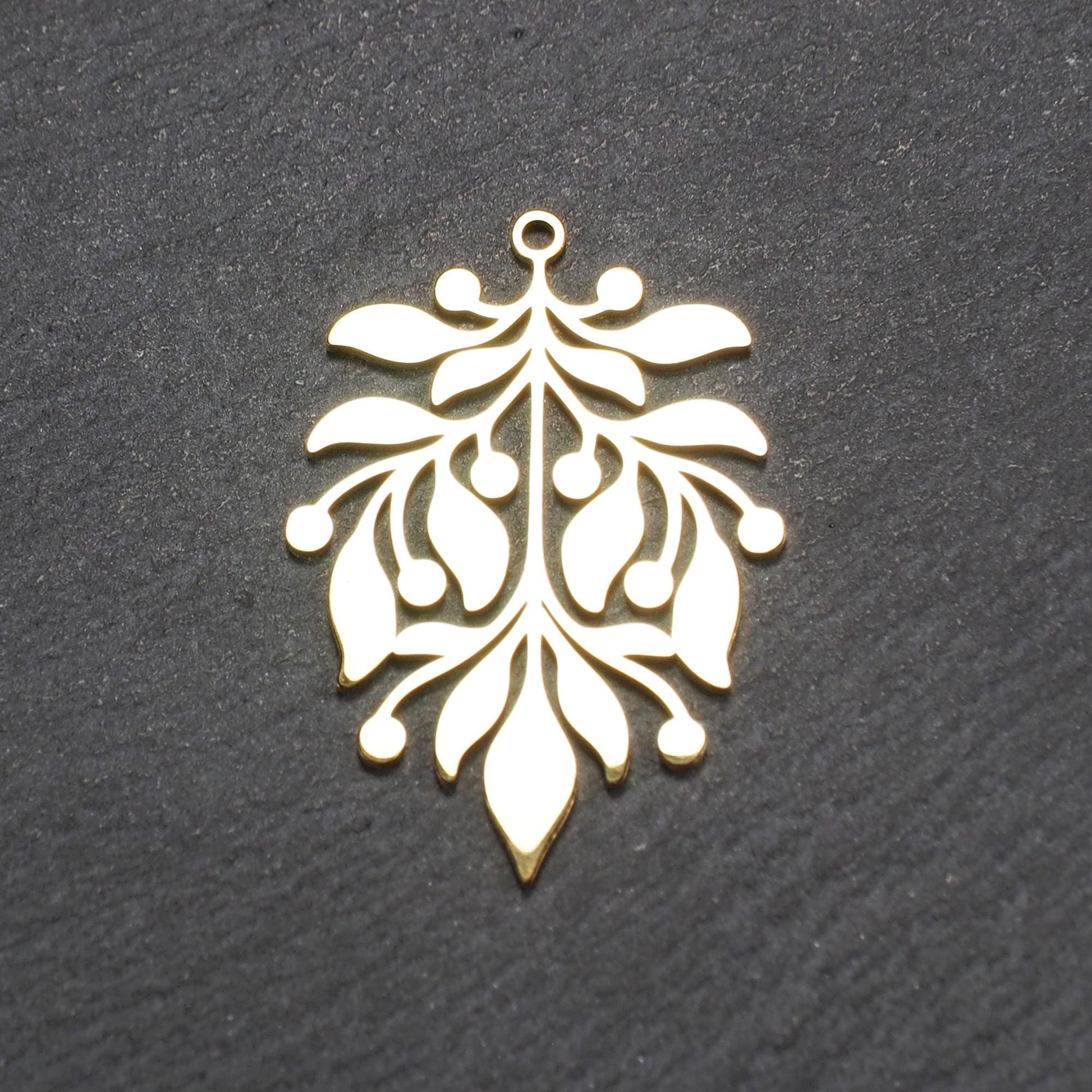 Goldfarbener Metallanhänger mit glänzender Oberfläche, durchbrochenes Zweig- und Beerenmotiv mit stilisierten Blättern und runder Öse oben.