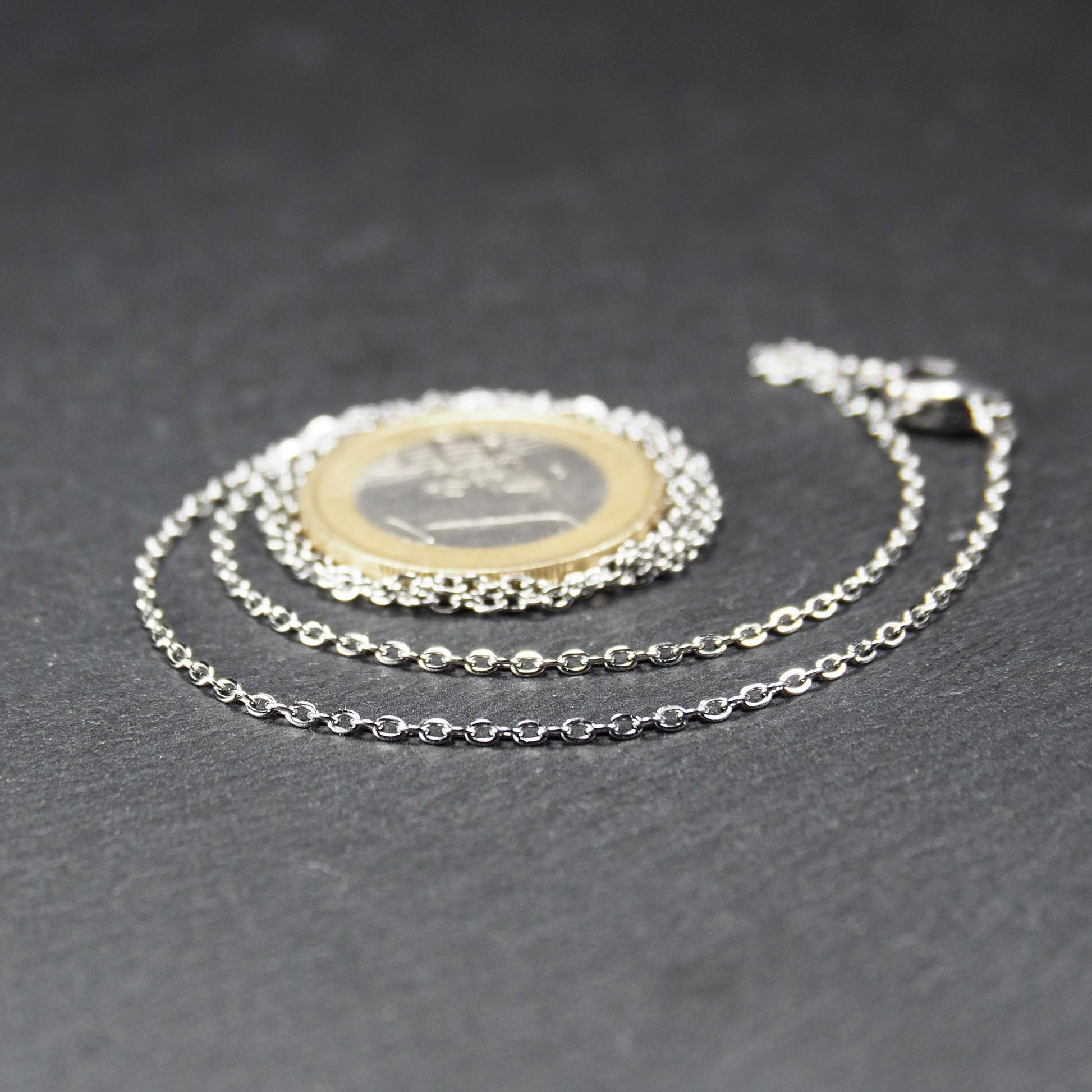 Eine Ankerkette hat filigrane offene Ankerglieder, polierte silberne Oberfläche und einen sichtbaren Karabinerverschluss.