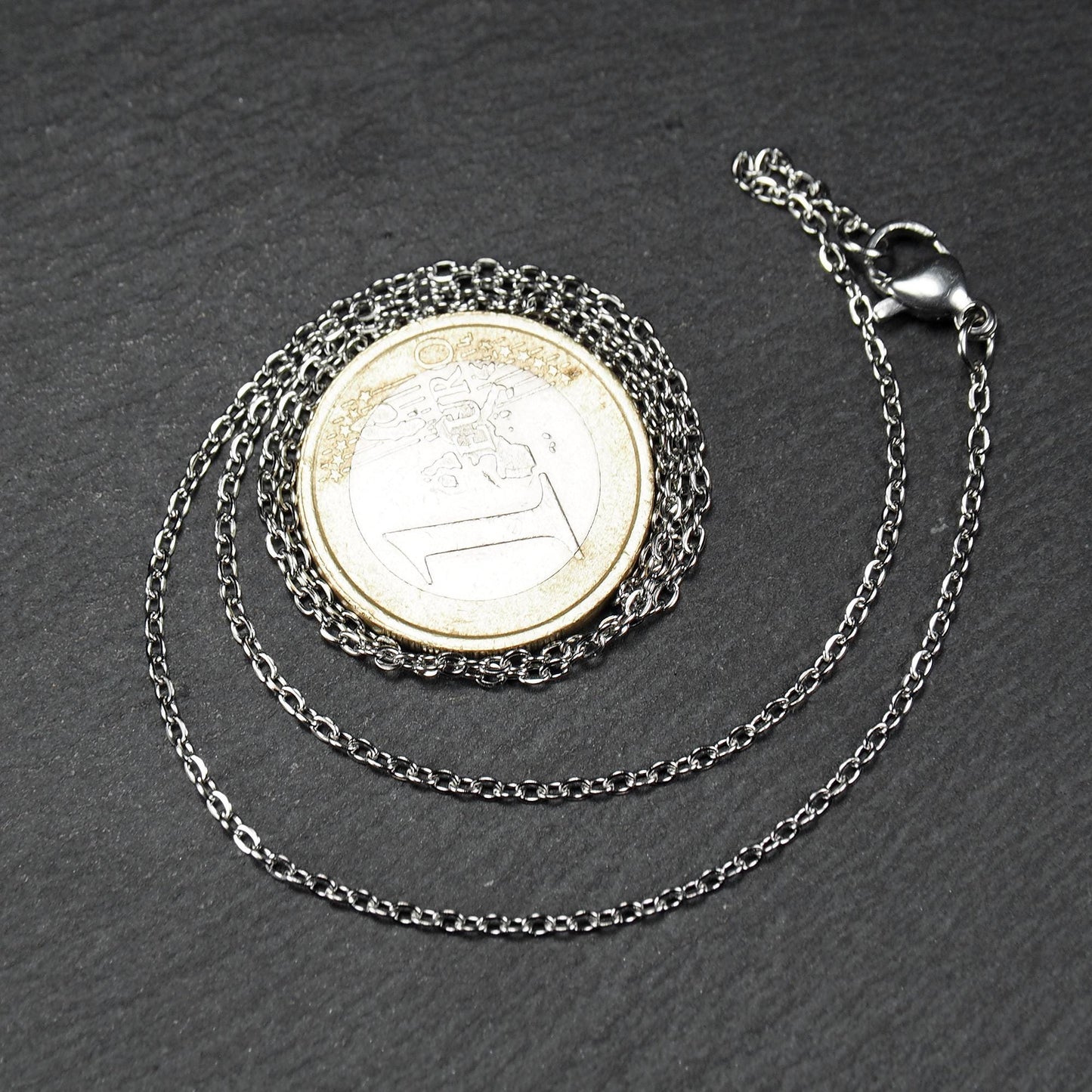 Eine Ankerkette hat filigrane offene Ankerglieder, polierte silberne Oberfläche und einen sichtbaren Karabinerverschluss.