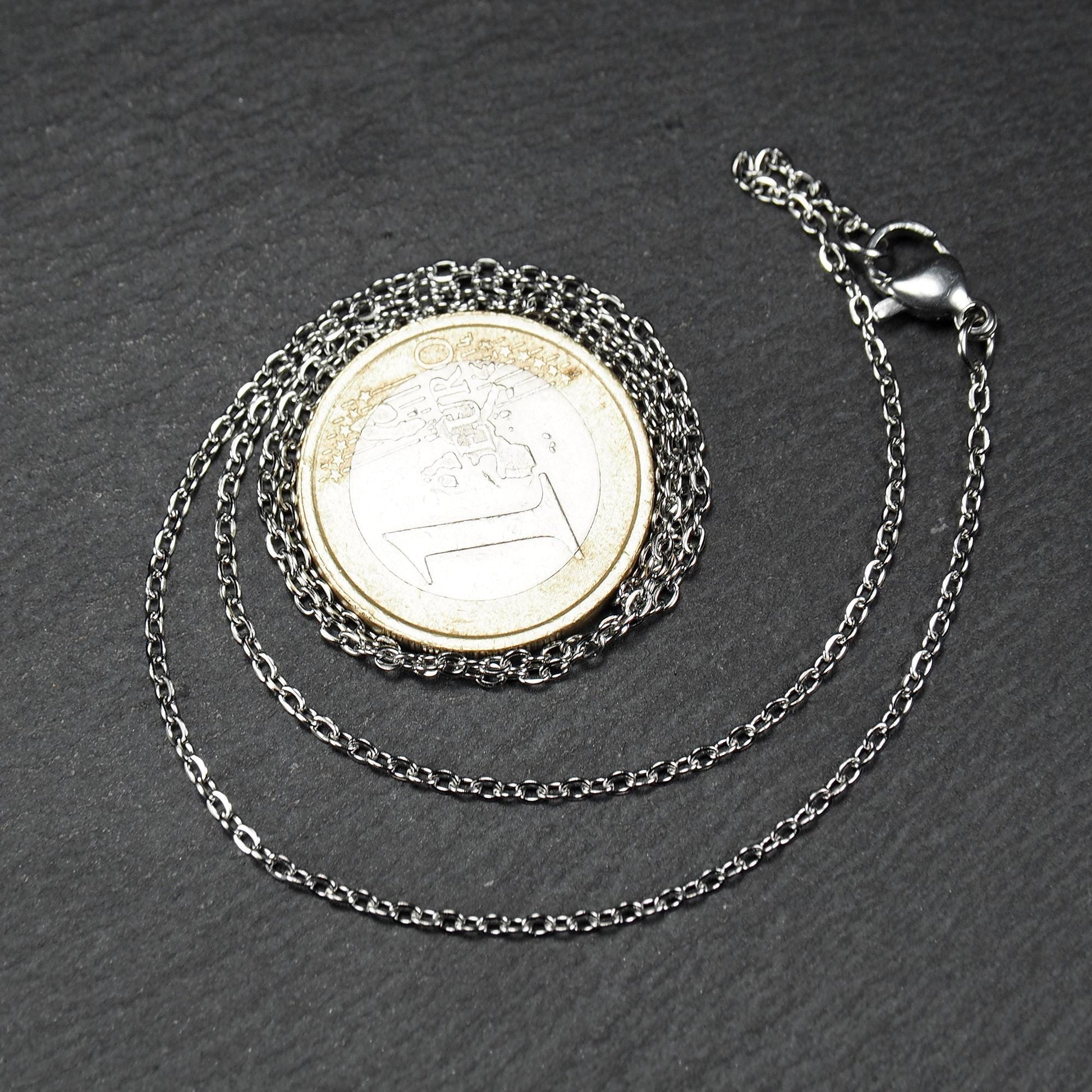 Eine Ankerkette hat filigrane offene Ankerglieder, polierte silberne Oberfläche und einen sichtbaren Karabinerverschluss.