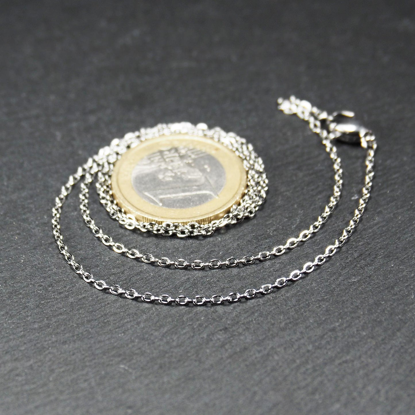 Eine Ankerkette hat filigrane offene Ankerglieder, polierte silberne Oberfläche und einen sichtbaren Karabinerverschluss.