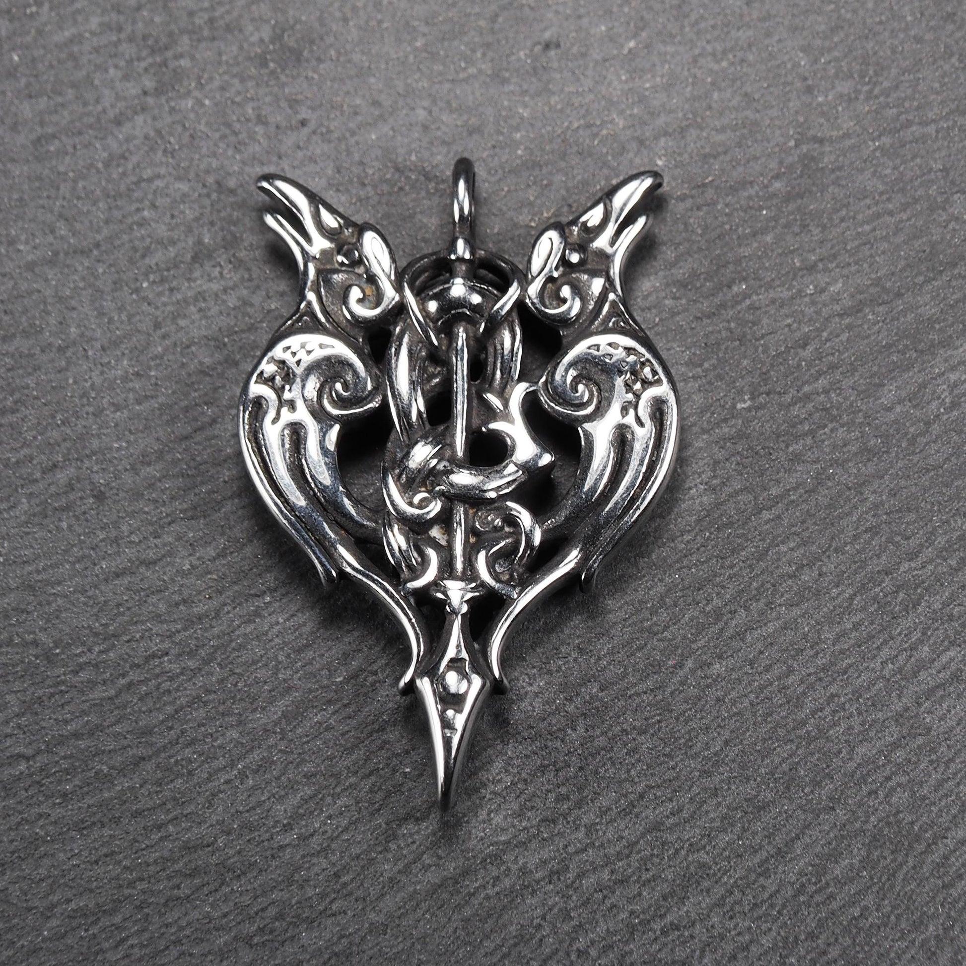 Anhänger aus poliertem silberfarbenem Edelstahl, zweiköpfiges, spitz zulaufendes Rabenschwert Ornament mit Relief, Durchbrüchen und sichtbarer Öse.