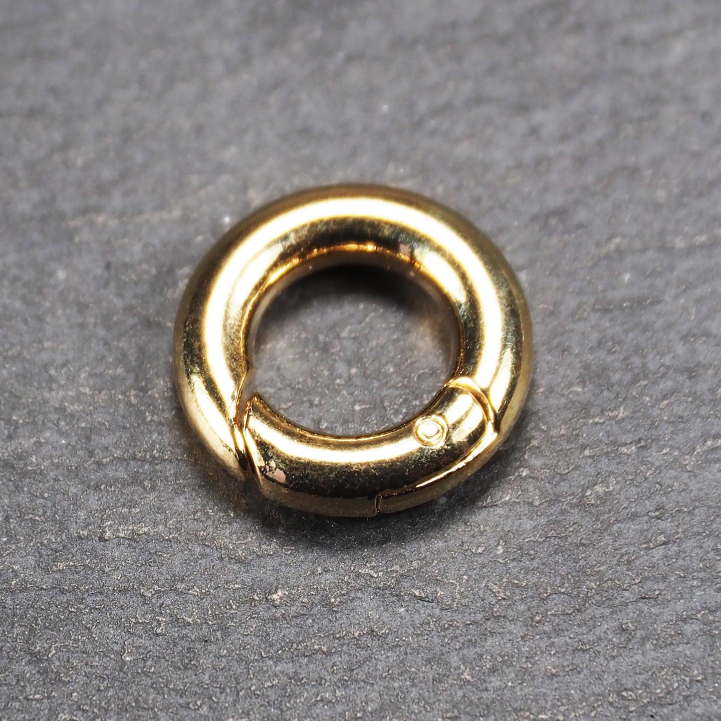 Runder vergoldeter O-Ring Karabiner mit glänzender Oberfläche, torusförmiger Öffnung und sichtbarem Schnappverschluss mit Scharnier.