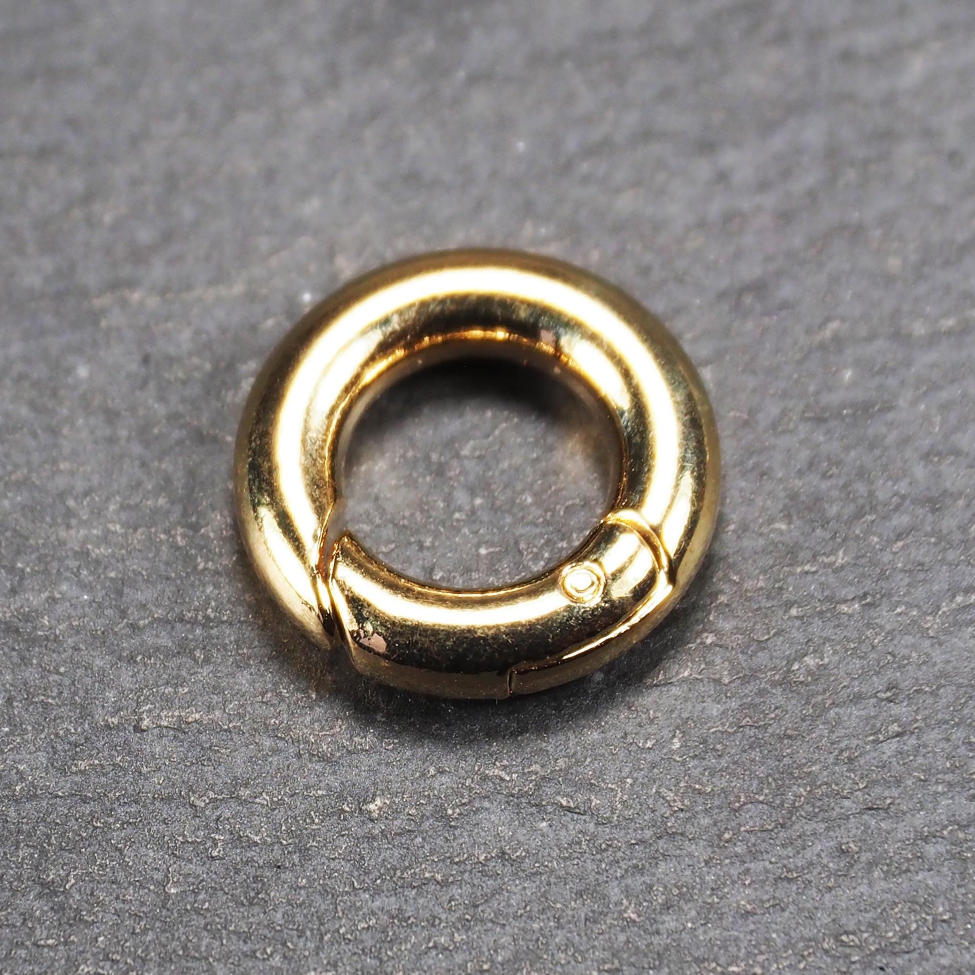 Runder vergoldeter O-Ring Karabiner mit glänzender Oberfläche, torusförmiger Öffnung und sichtbarem Schnappverschluss mit Scharnier.