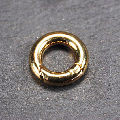 Runder vergoldeter O-Ring Karabiner mit glänzender Oberfläche, torusförmiger Öffnung und sichtbarem Schnappverschluss mit Scharnier.