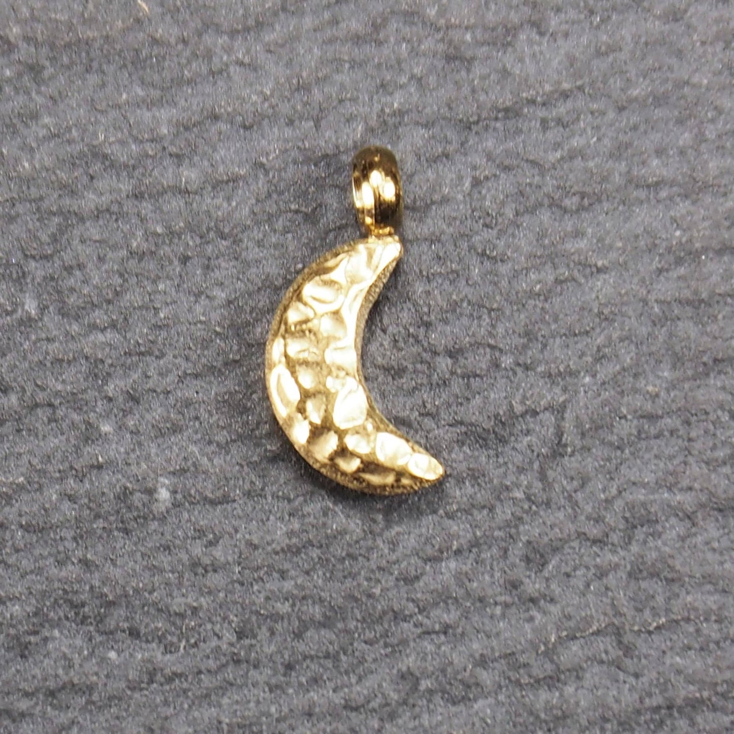 Halbmond-Anhänger, goldfarben und glänzend, reliefartige gehämmerte Textur, organisch geschwungene Mondsichelform mit kleiner Öse oben.