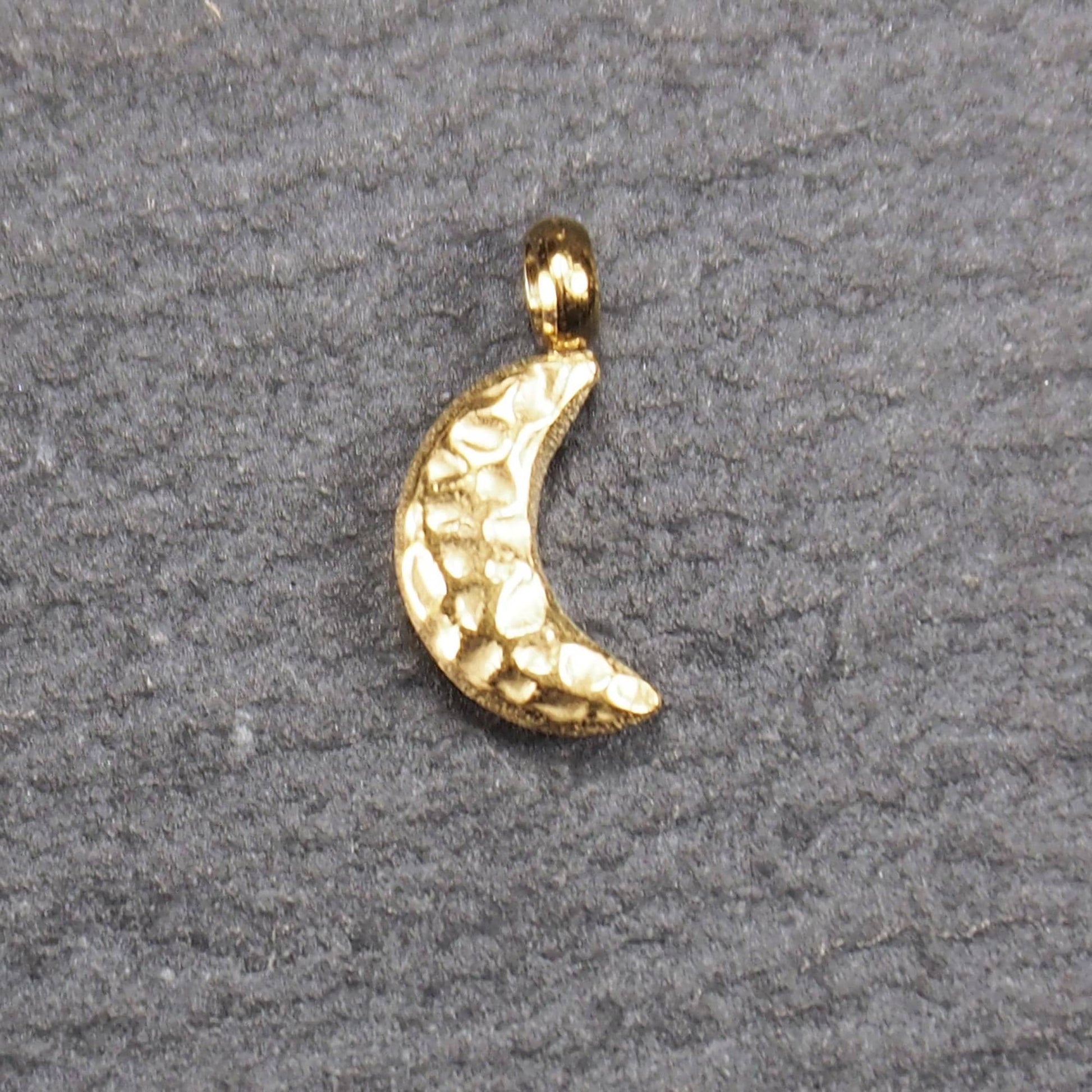 Halbmond-Anhänger, goldfarben und glänzend, reliefartige gehämmerte Textur, organisch geschwungene Mondsichelform mit kleiner Öse oben.