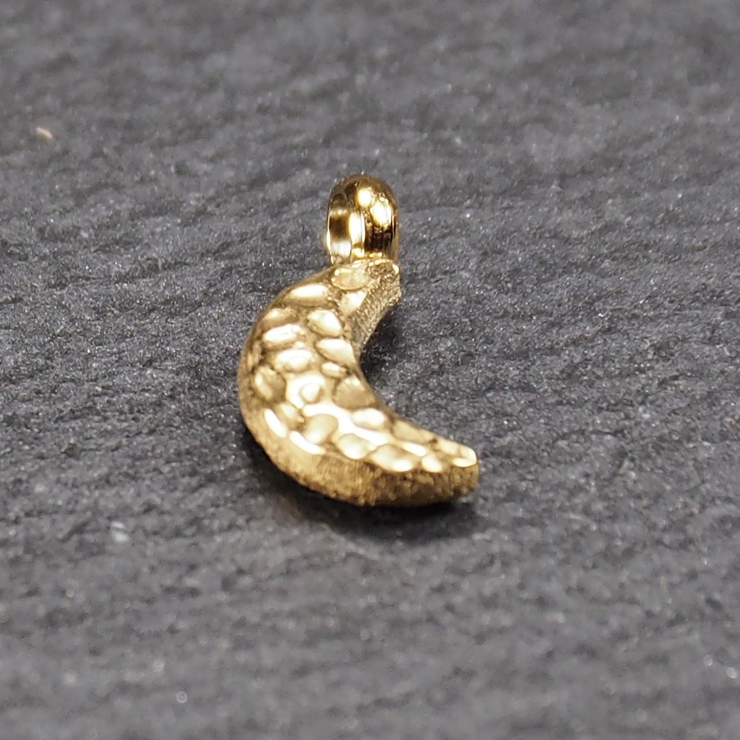 Halbmond-Anhänger, goldfarben und glänzend, reliefartige gehämmerte Textur, organisch geschwungene Mondsichelform mit kleiner Öse oben.