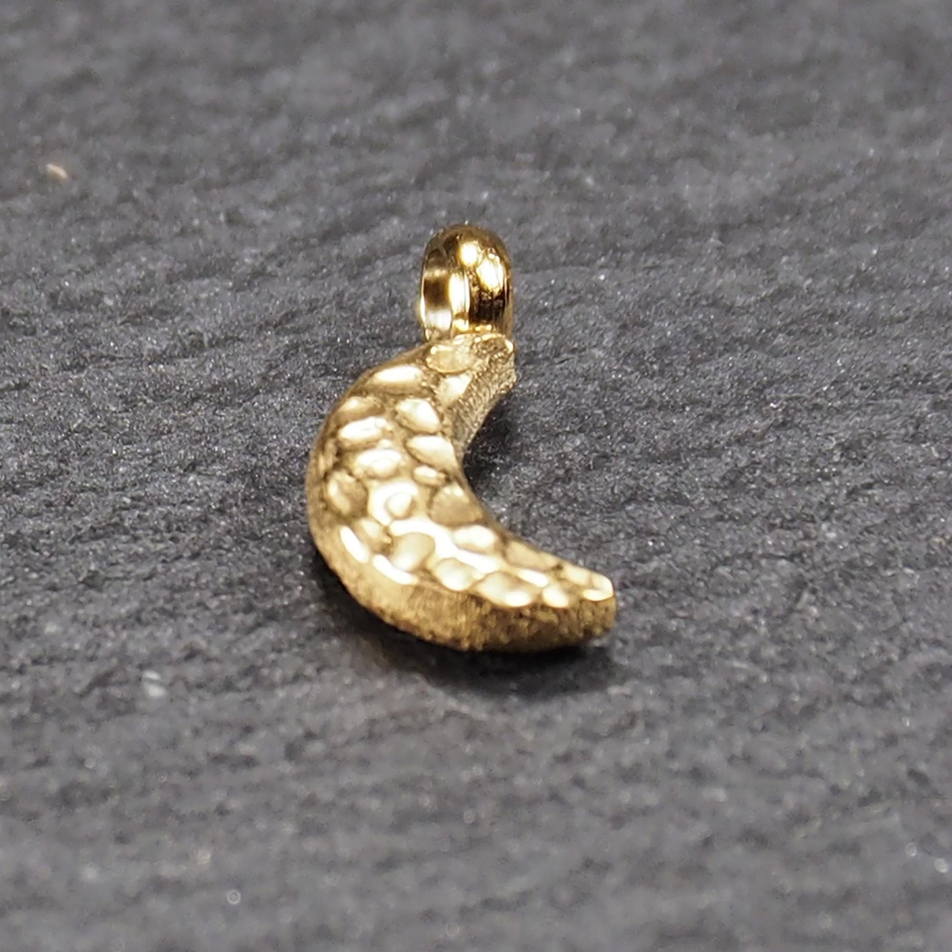 Halbmond-Anhänger, goldfarben und glänzend, reliefartige gehämmerte Textur, organisch geschwungene Mondsichelform mit kleiner Öse oben.