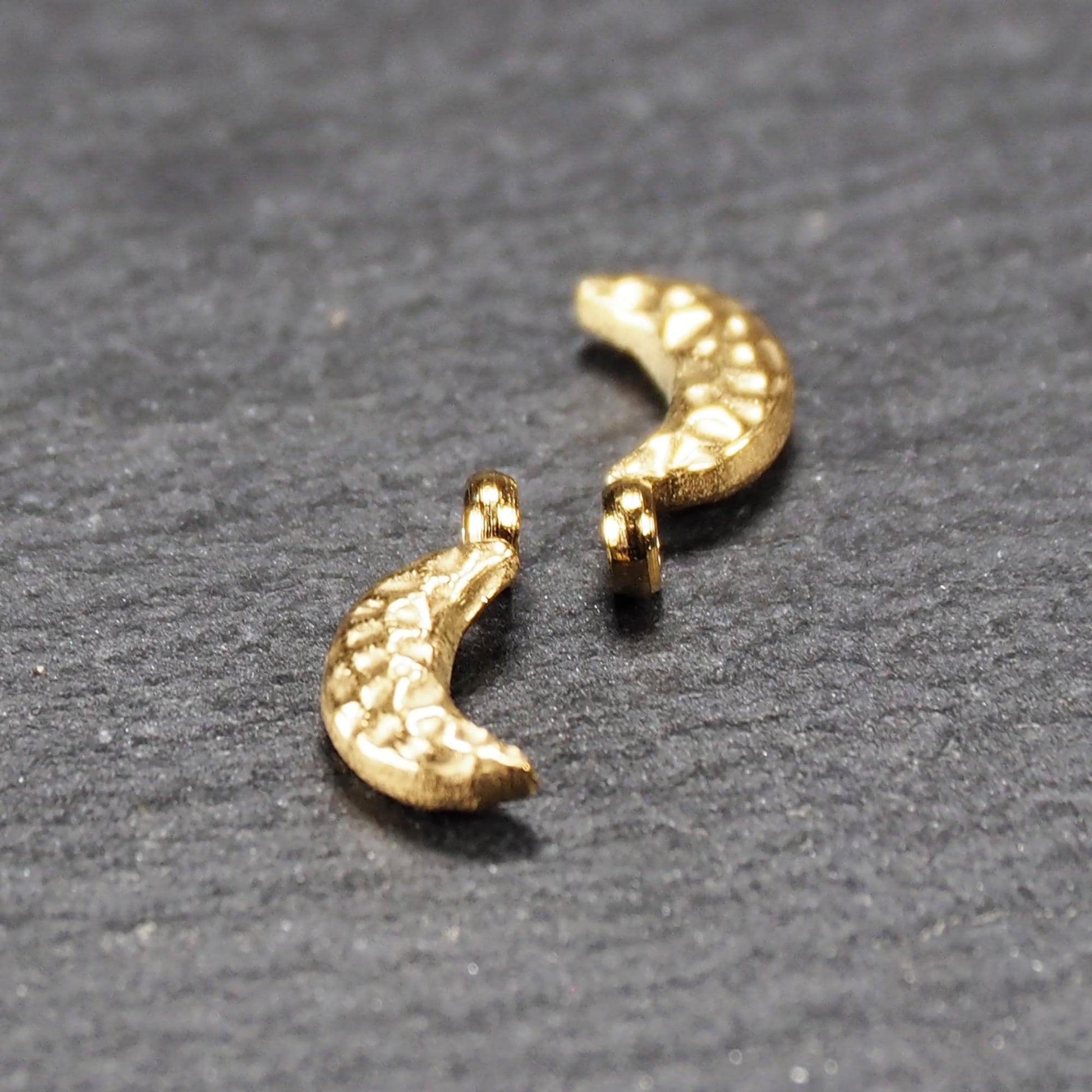 Halbmond-Anhänger, goldfarben und glänzend, reliefartige gehämmerte Textur, organisch geschwungene Mondsichelform mit kleiner Öse oben.