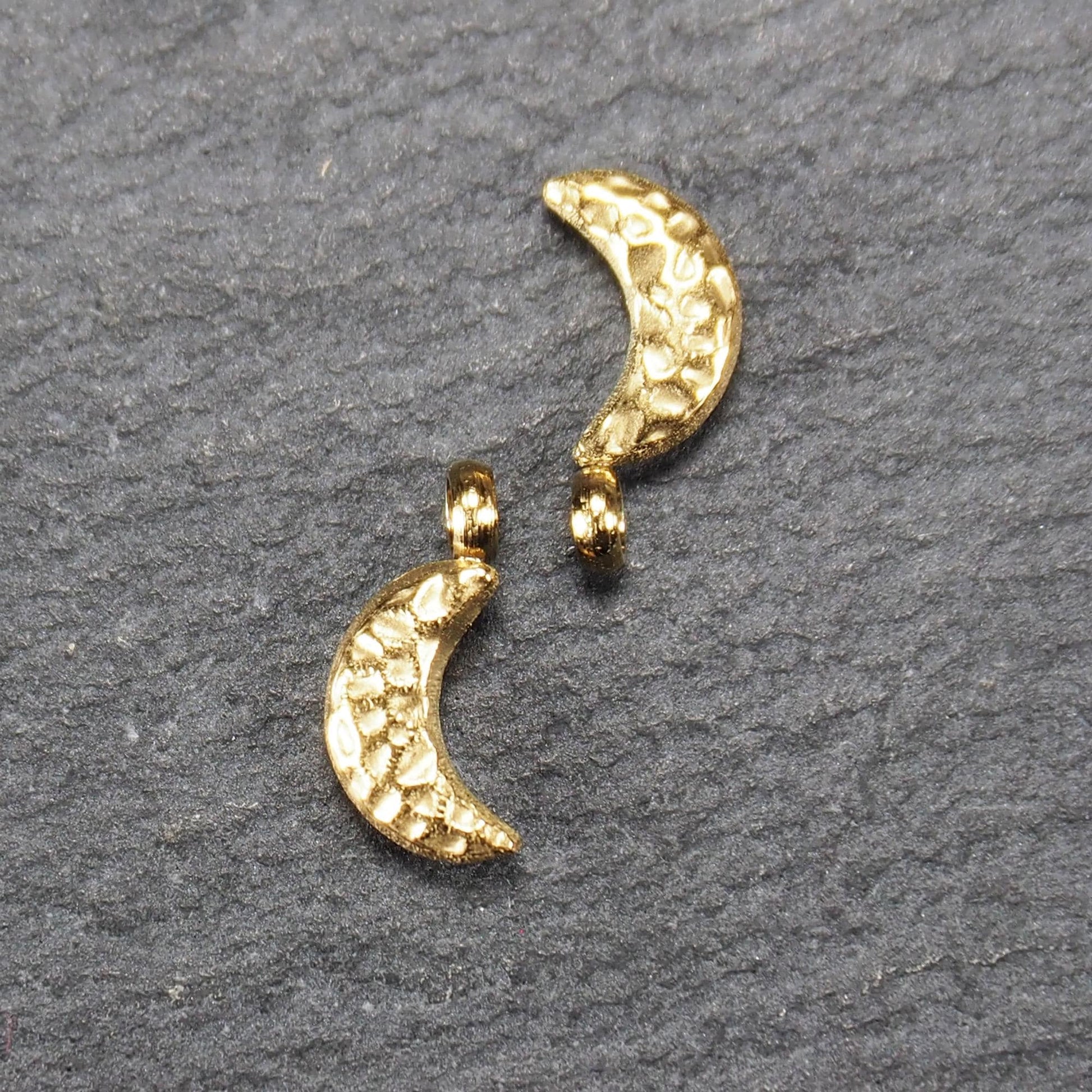 Halbmond-Anhänger, goldfarben und glänzend, reliefartige gehämmerte Textur, organisch geschwungene Mondsichelform mit kleiner Öse oben.