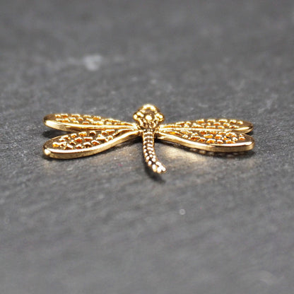 Libellen-Anhänger aus goldfarbenem, glänzendem Metall mit durchbrochenen, netzartigen Flügeln, schlankem segmentiertem Körper und kleiner runder Aufhängöse.